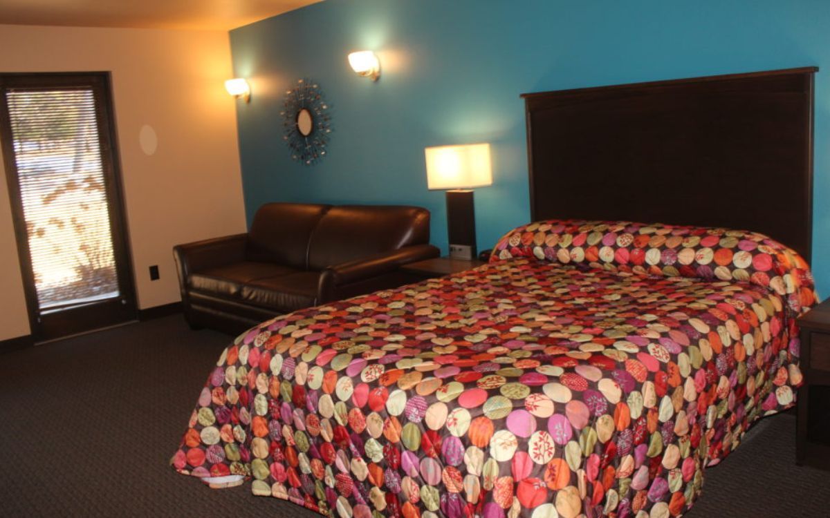 Hotel room with a bed, small sofa, and a door, teal wall.