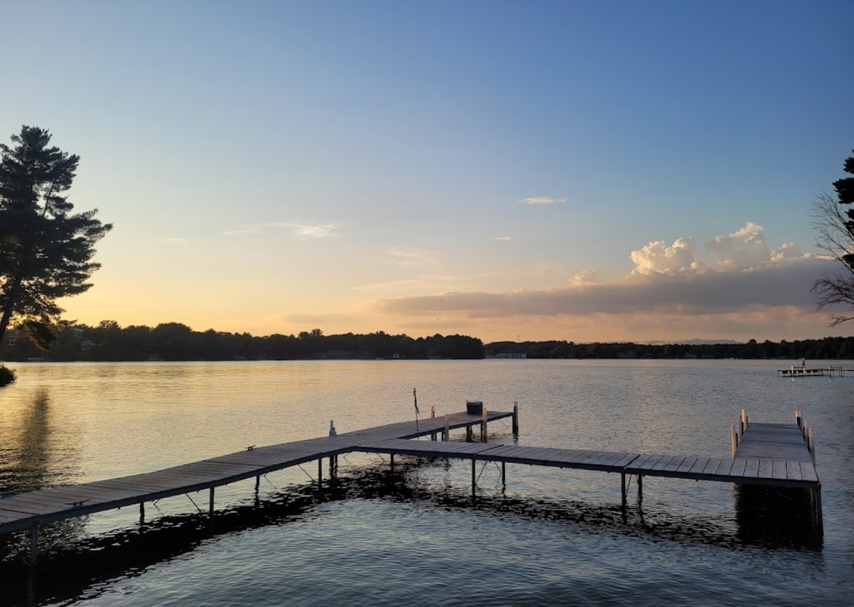 Wooden docks extending into a calm lake at sunset. Orange and blue sky, trees on the horizon.