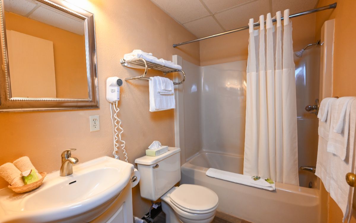 Bathroom with sink, toilet, tub, and towels; walls are peach colored.