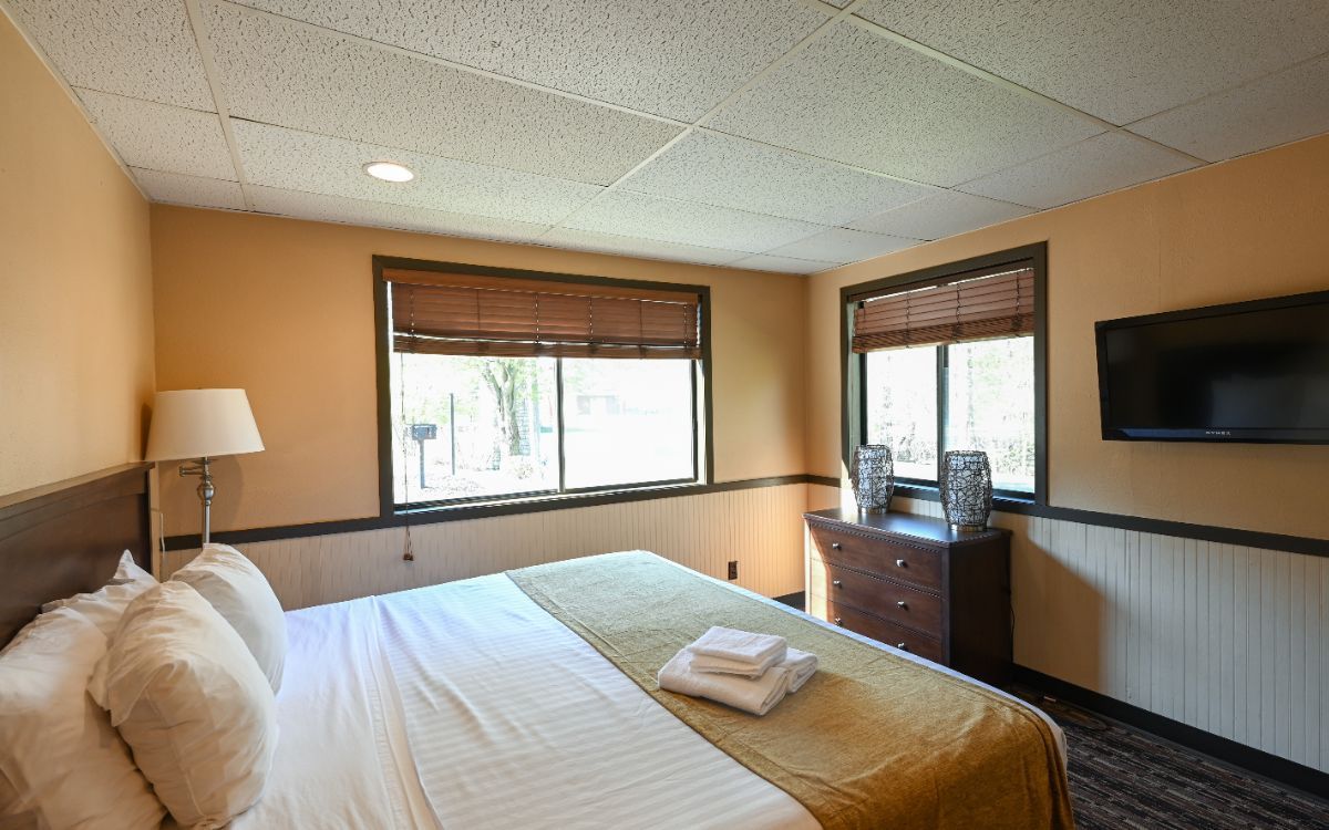 Bedroom with a large bed, TV, and two windows. Walls are painted tan and off-white.