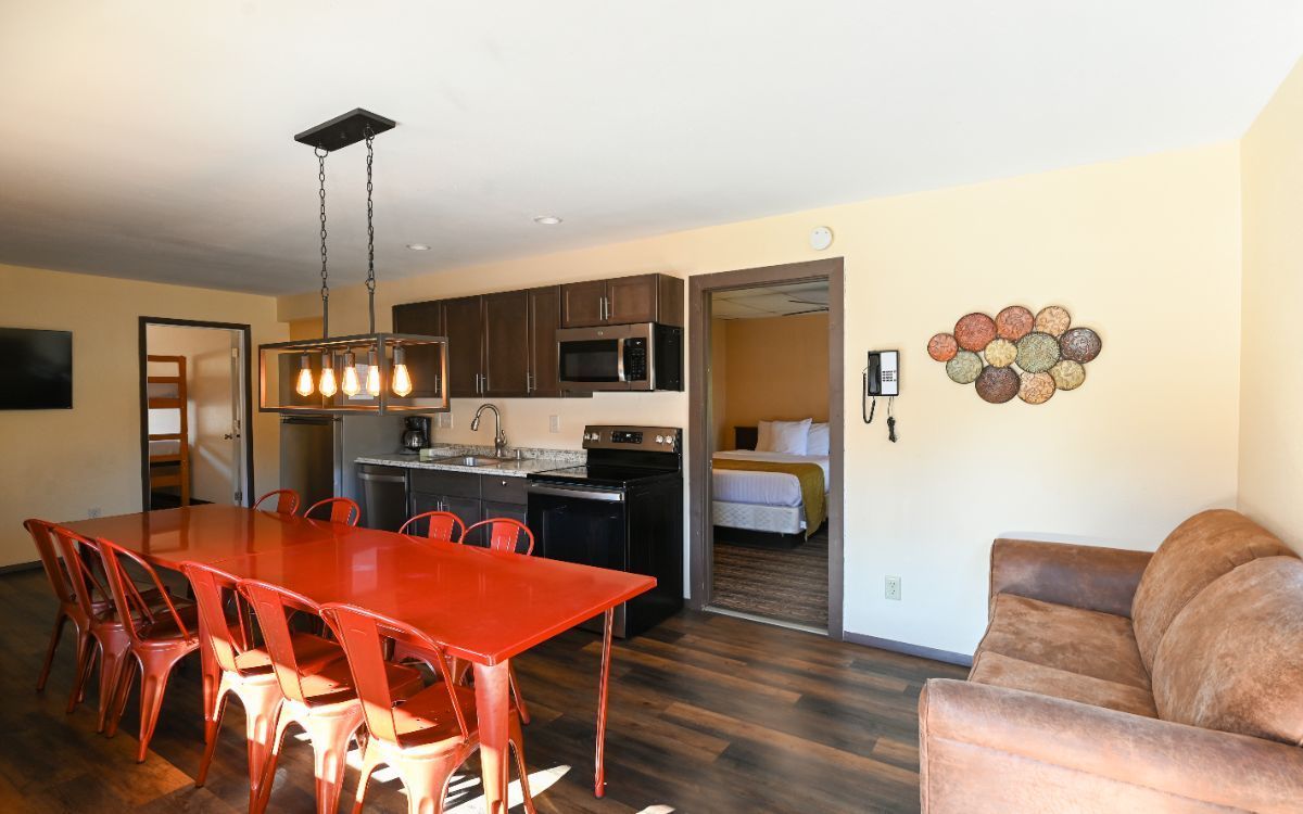 An open-concept living space with a red table, kitchen, couch, and bedroom.