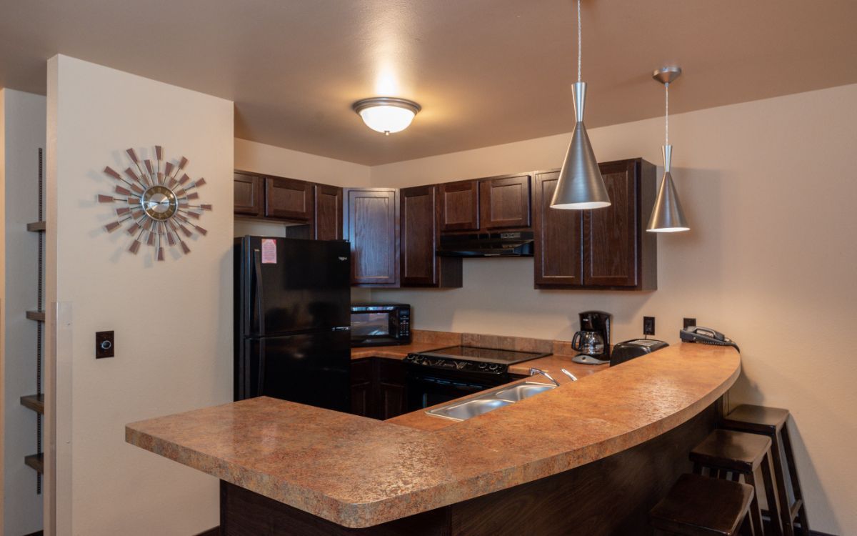 Kitchen with brown cabinets, black appliances, and a curved countertop. Two pendant lights hang over the counter.
