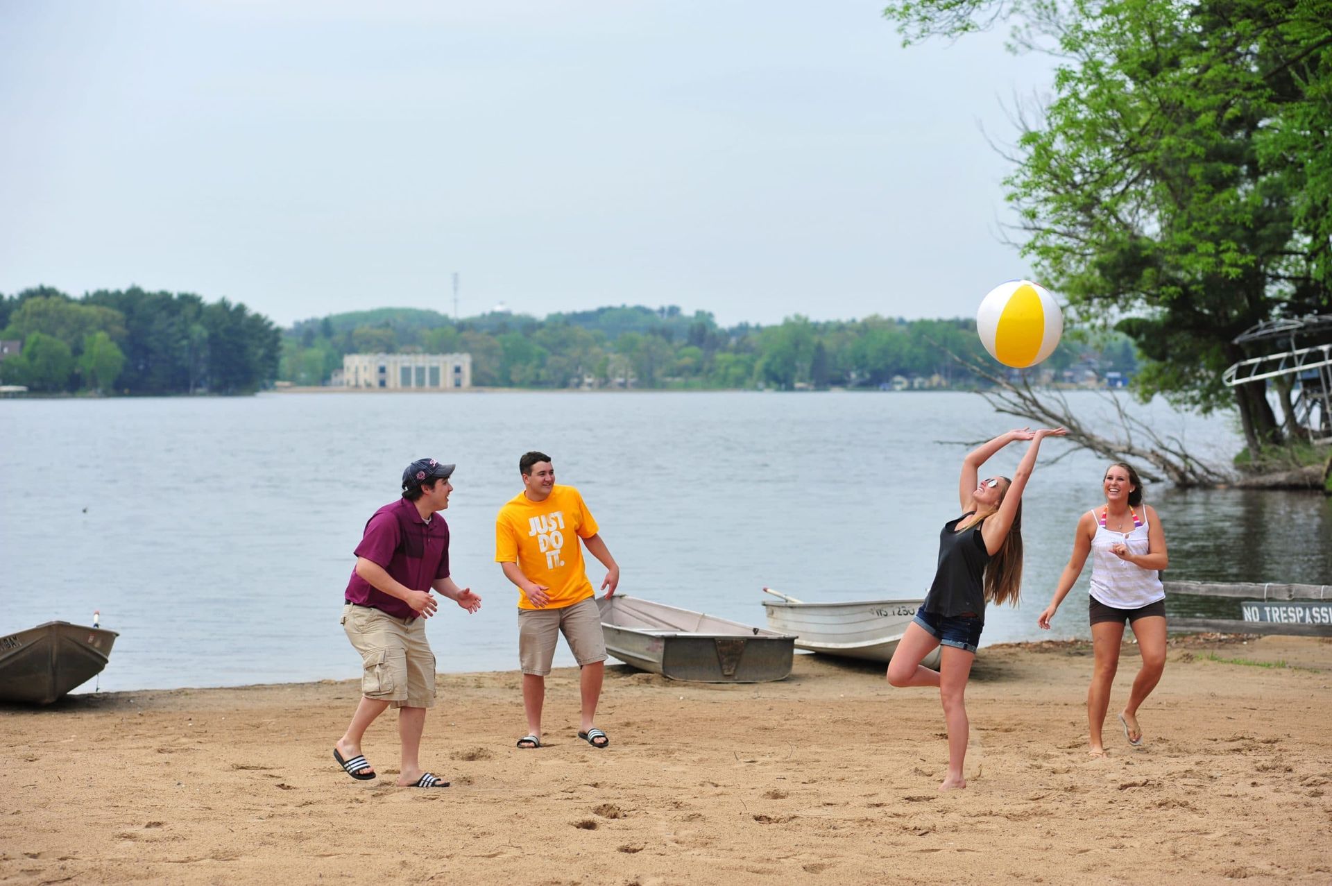 People playing beach volleyball on a sandy shore near a lake.