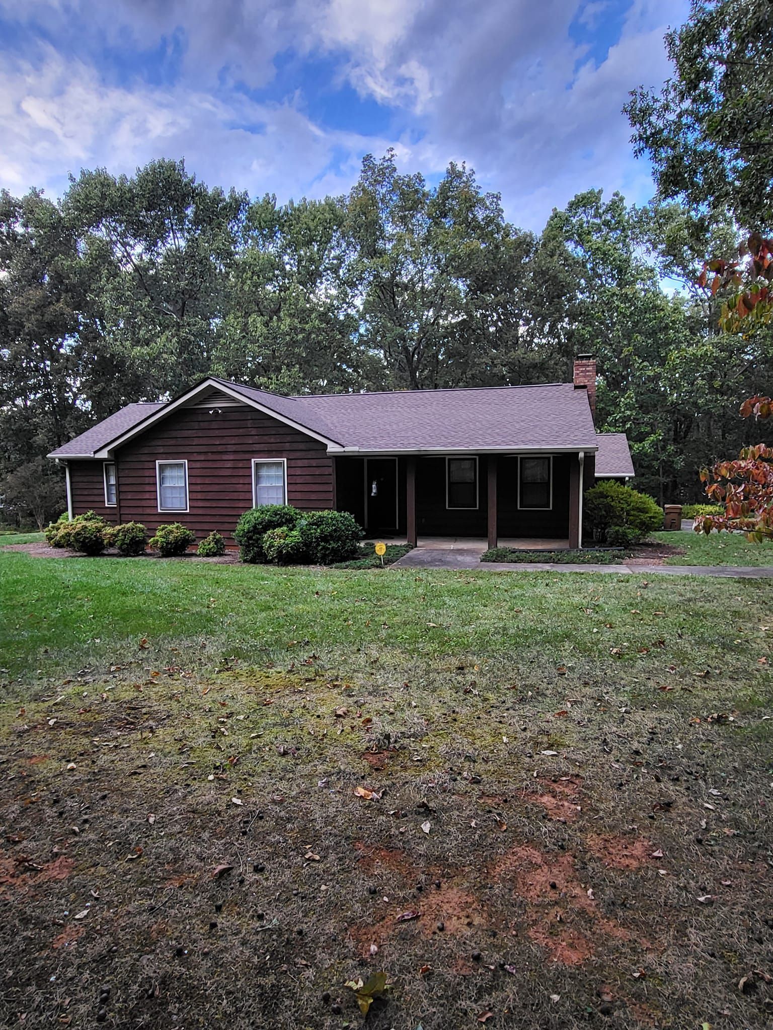 A brown house with a gray roof sits in the middle of a lush green field