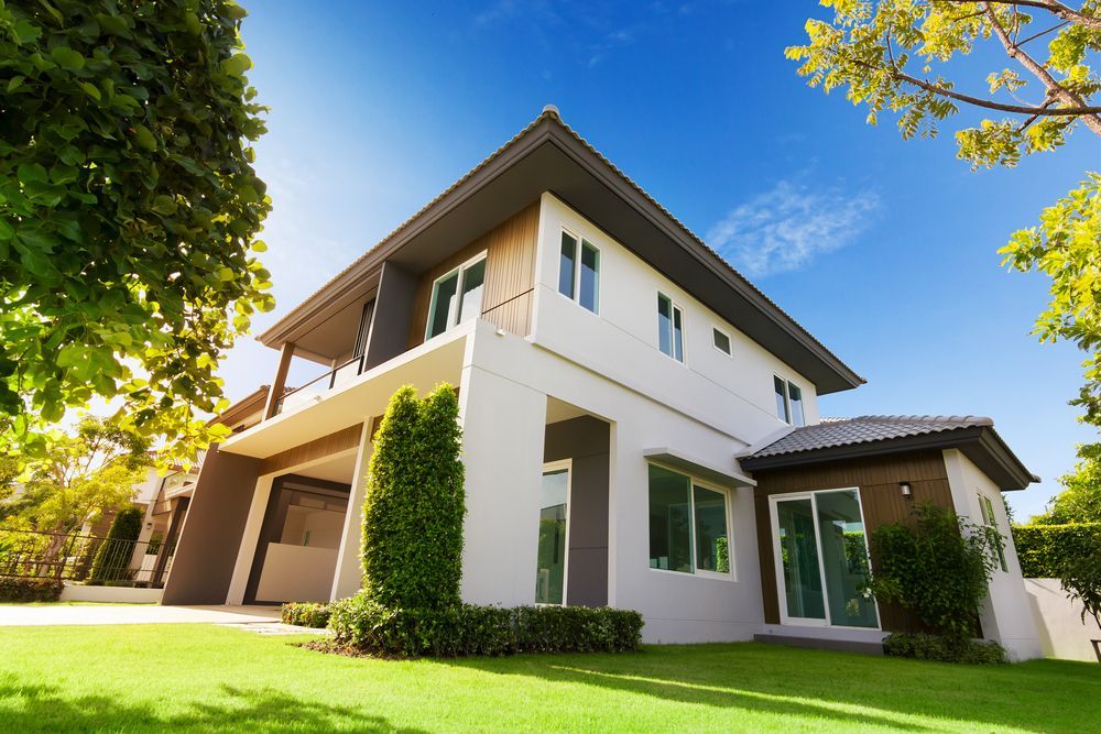 Modern two-story house with green lawn and blue sky. Features a garage and balcony.