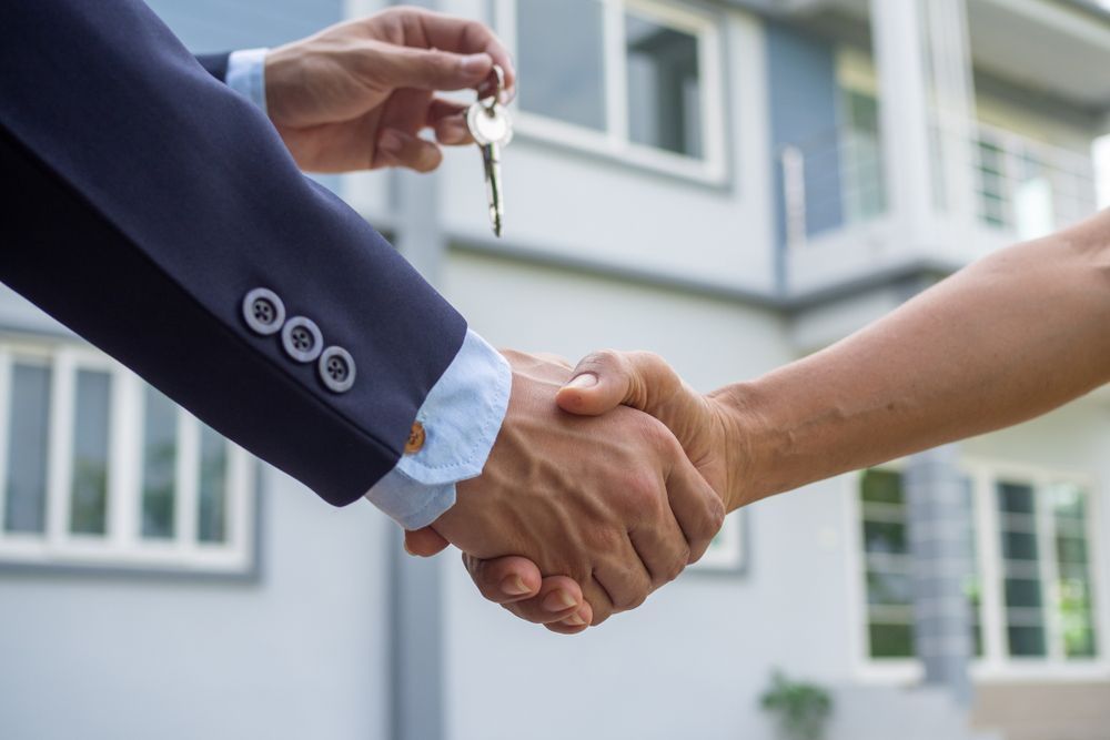 Person handing keys and shaking hands in front of a house.