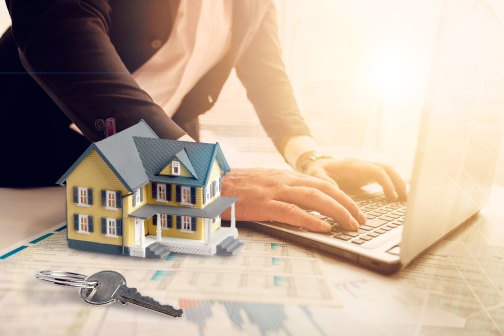 Miniature house, keys, and person working on a laptop, likely in a real estate context.
