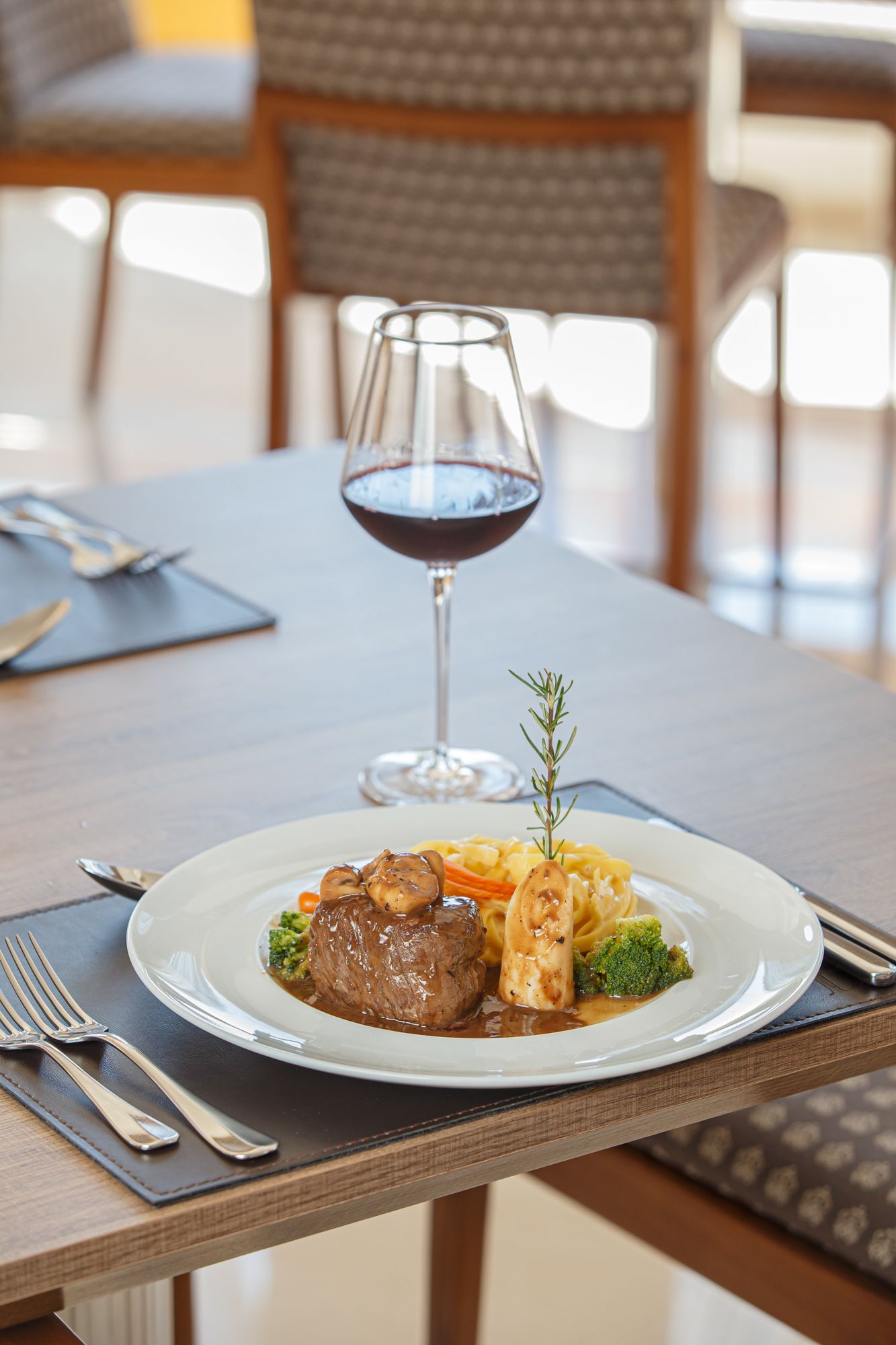 Carré de cordeiro em um prato branco com legumes e molho, apresentado em um ambiente de restaurante.