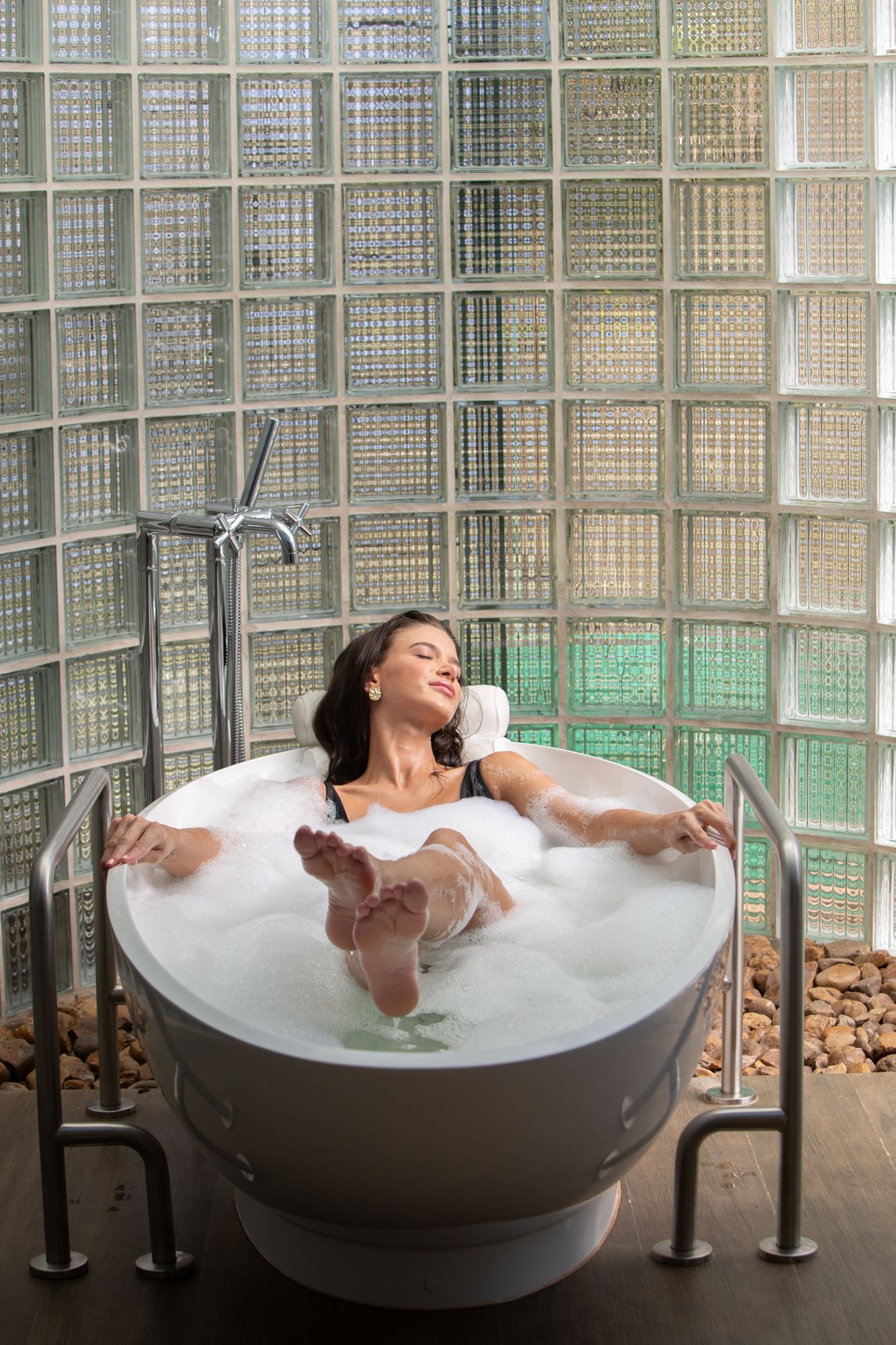Mulher em uma sauna, enrolada em uma toalha branca, relaxando com os olhos fechados, interior de madeira.