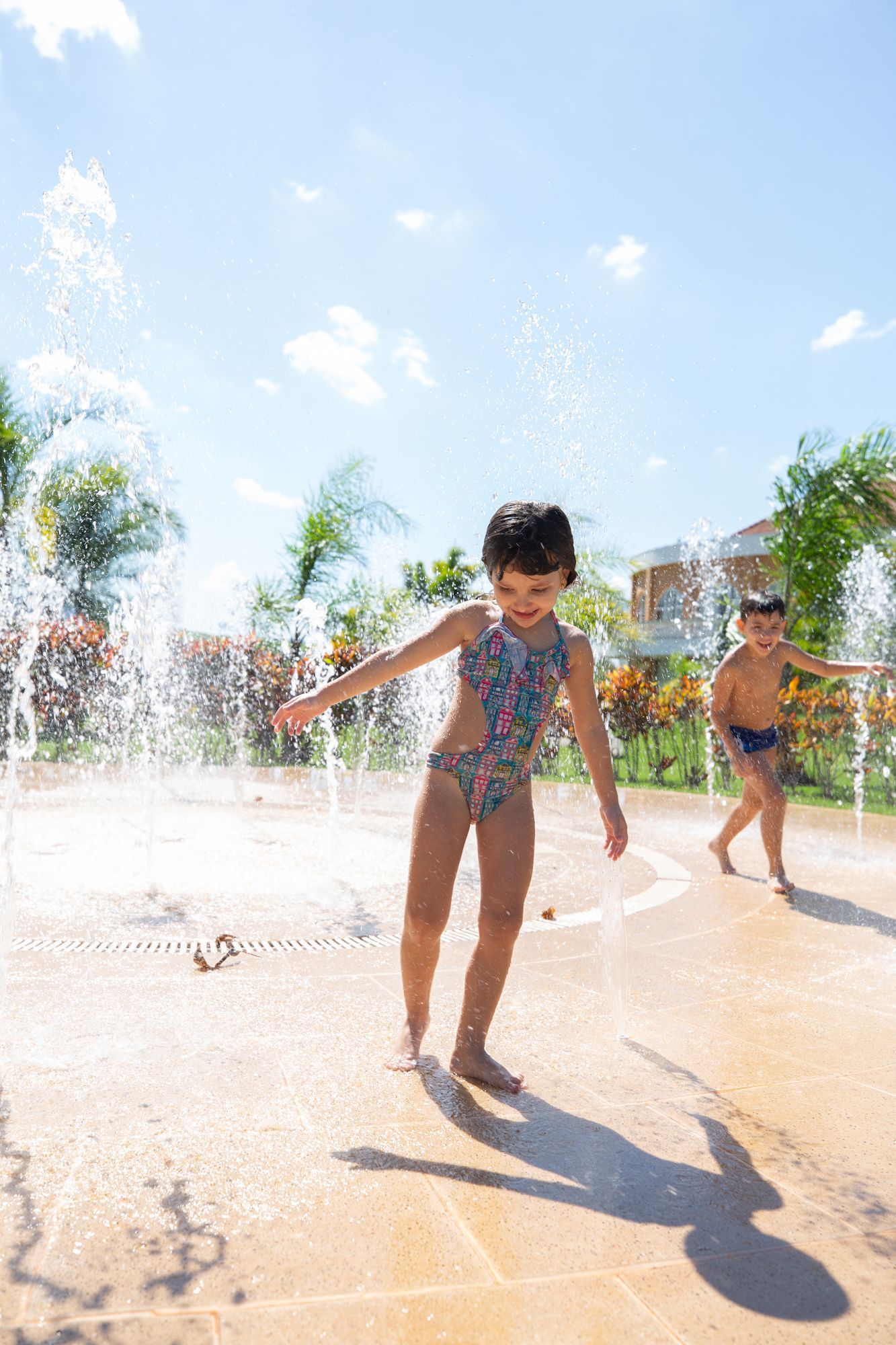 Piscina em um resort tropical com espreguiçadeiras, palmeiras e prédios sob um céu azul.
