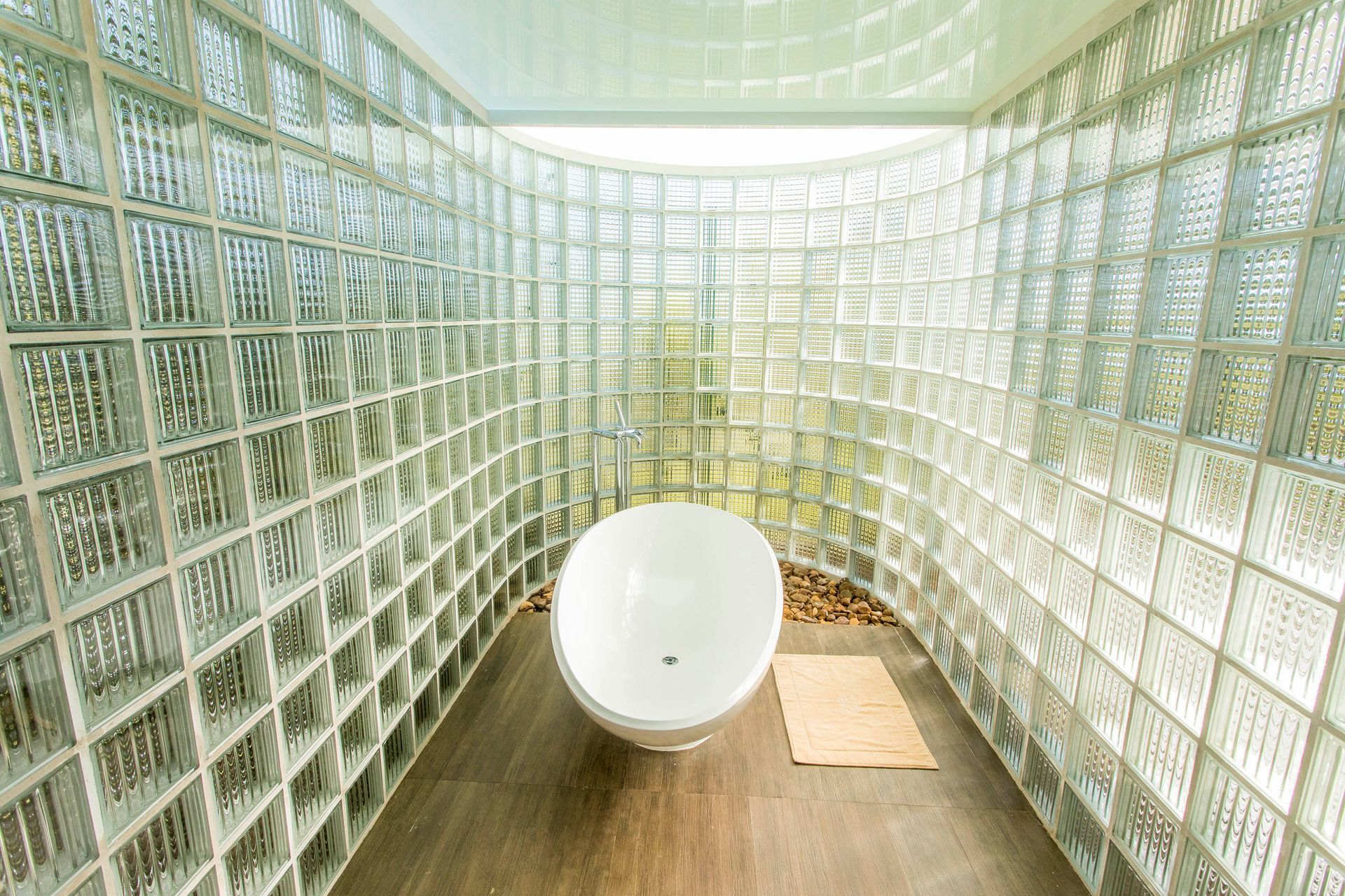 Mulher recebendo uma máscara facial aplicada com um pincel; roupão branco, olhos fechados.