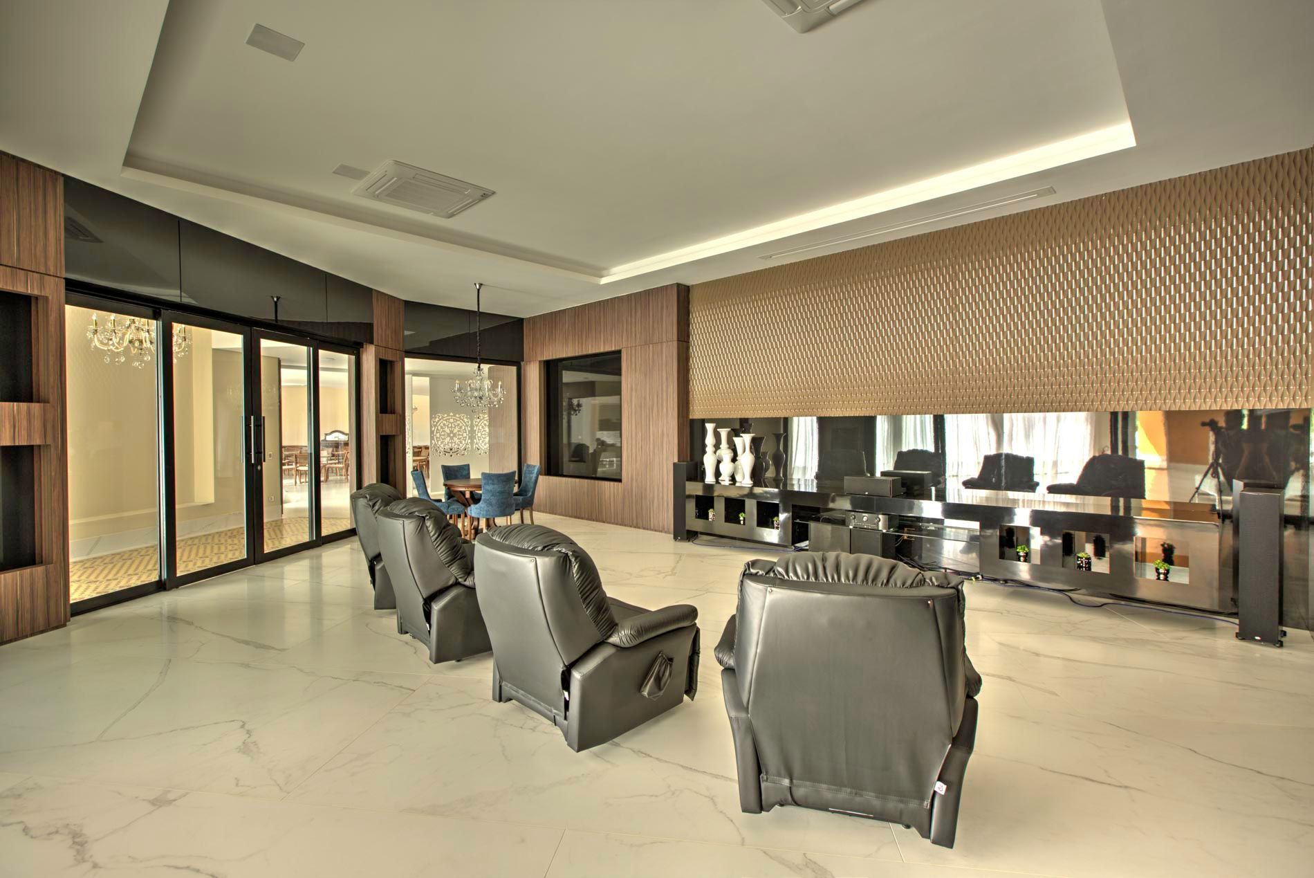 Lounge moderno com poltronas reclináveis, detalhes em madeira e piso de mármore.