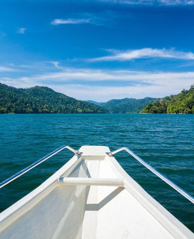 Barco navegando em águas azuis, colinas verdejantes ao longe sob um céu azul brilhante.