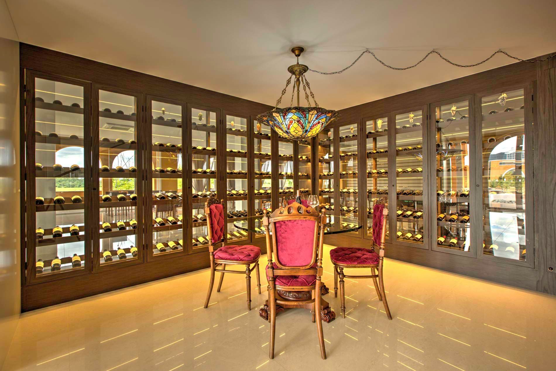 Adega com armários de vidro, mesa, cadeiras e um lustre colorido.