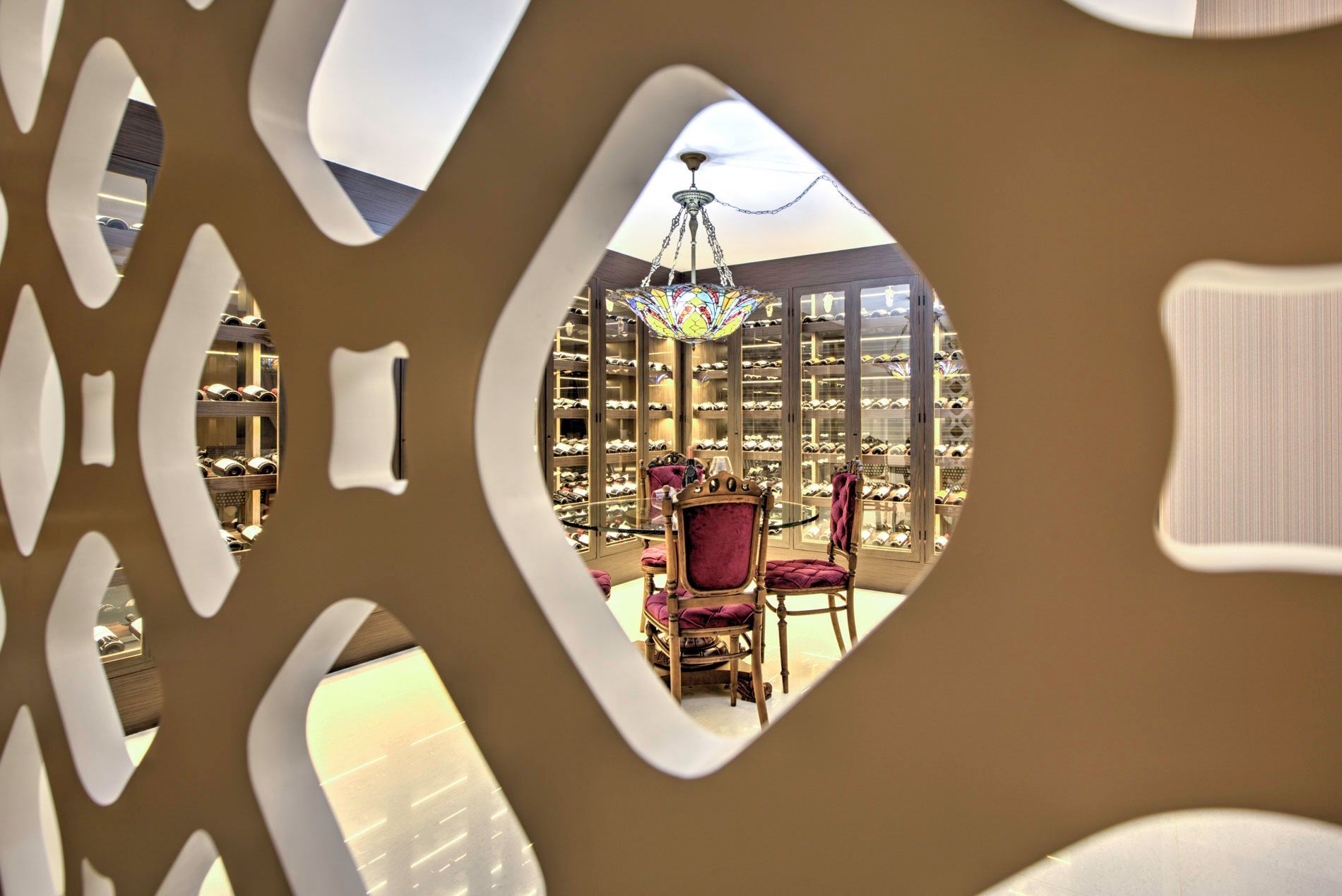 Uma divisória com padrão bege emoldura uma adega com um lustre, assentos e prateleiras de vinho.