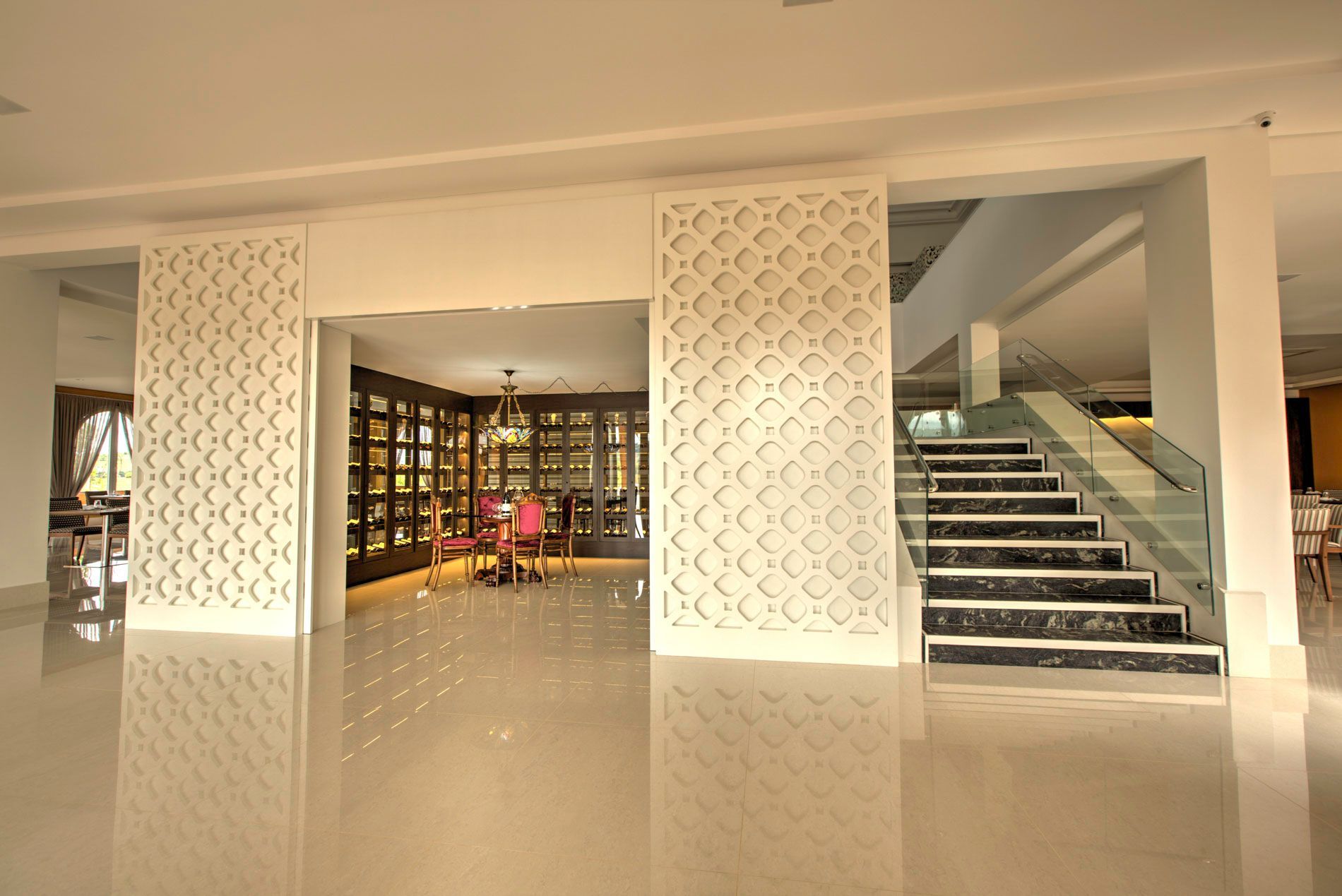 Interior iluminado com telas brancas decorativas, uma escada e um vislumbre de uma sala com cadeiras e prateleiras.