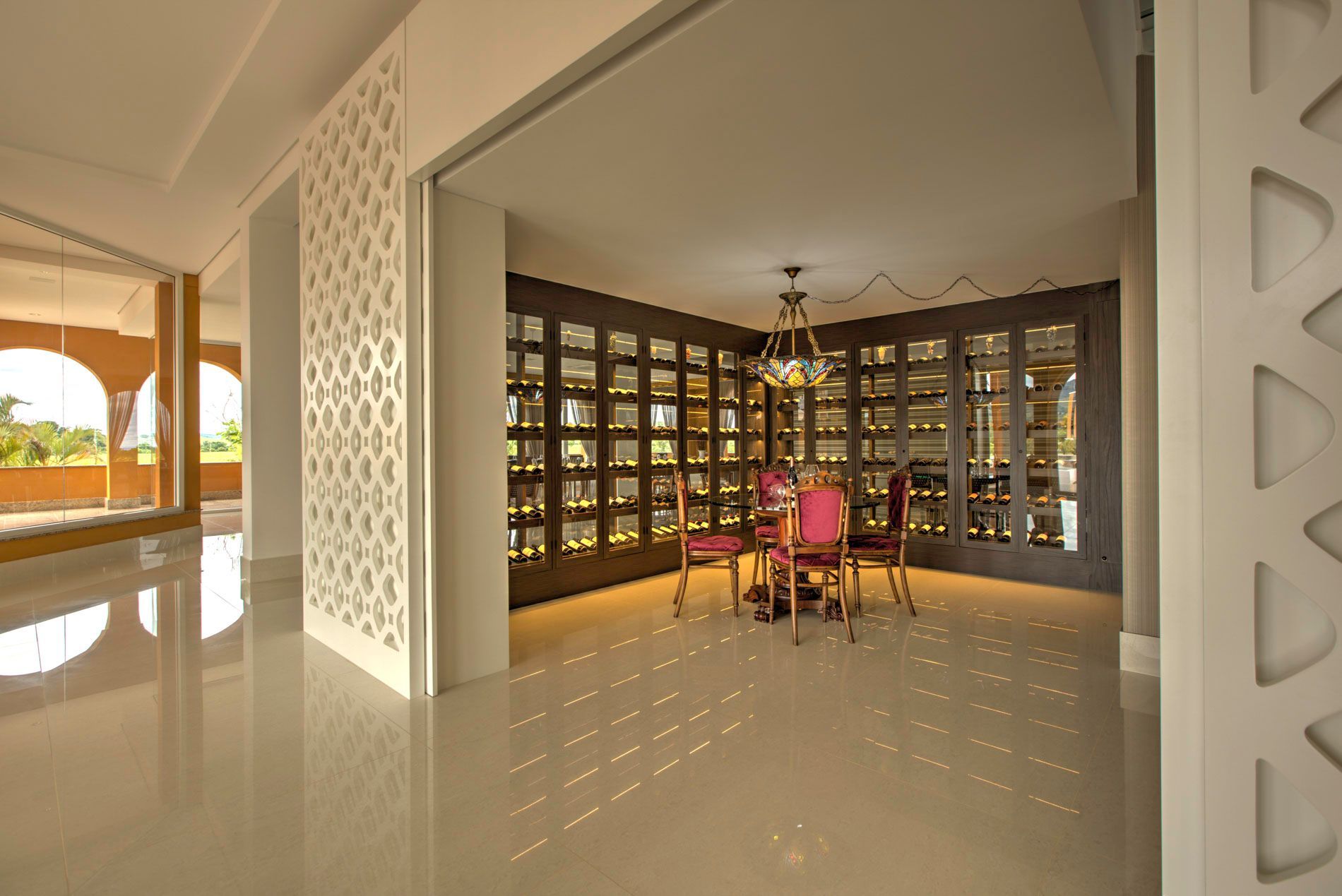 Uma sala de jantar com adega. A luz forte reflete no piso branco e brilhante.