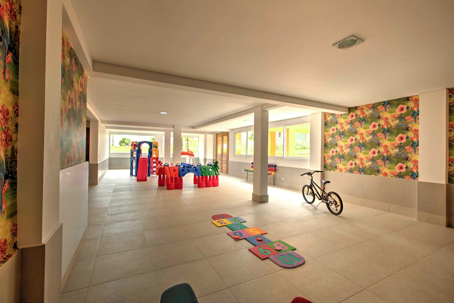 Sala de jogos interna com estruturas coloridas, bicicleta e papel de parede floral.