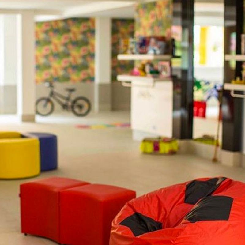 Uma sala de jogos iluminada e colorida com pufes, assentos em formato de cubo e uma bicicleta infantil em paredes estampadas.