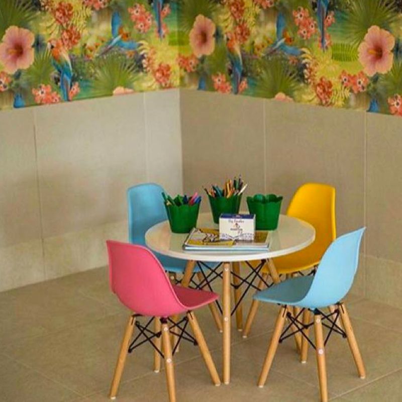 Uma área de recreação infantil com uma mesa redonda branca, cadeiras coloridas e papel de parede floral.