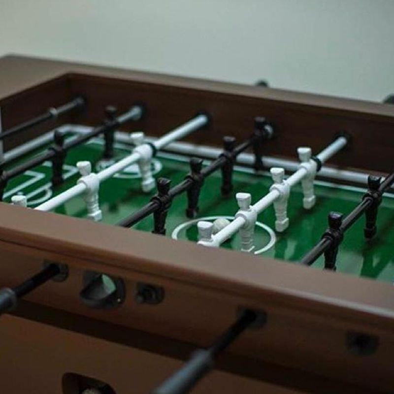 Mesa de pebolim com jogadores pretos e brancos em um campo verde, estrutura de mesa marrom.