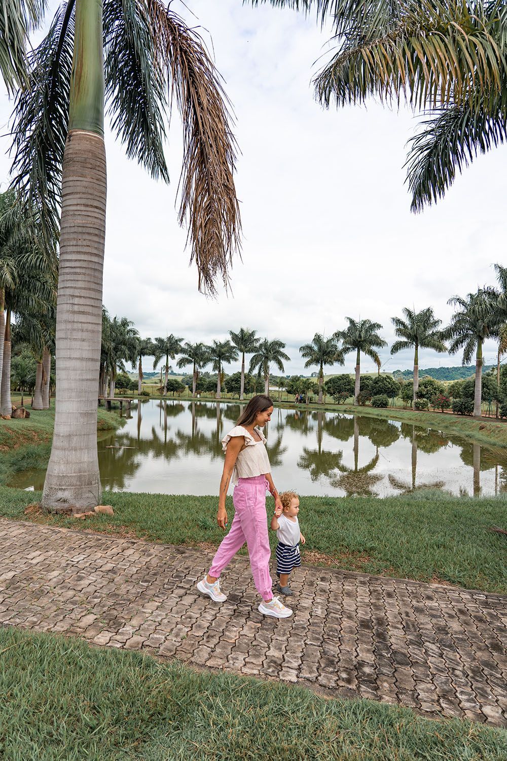 Mulher e criança caminhando em uma trilha perto de um lago com palmeiras.