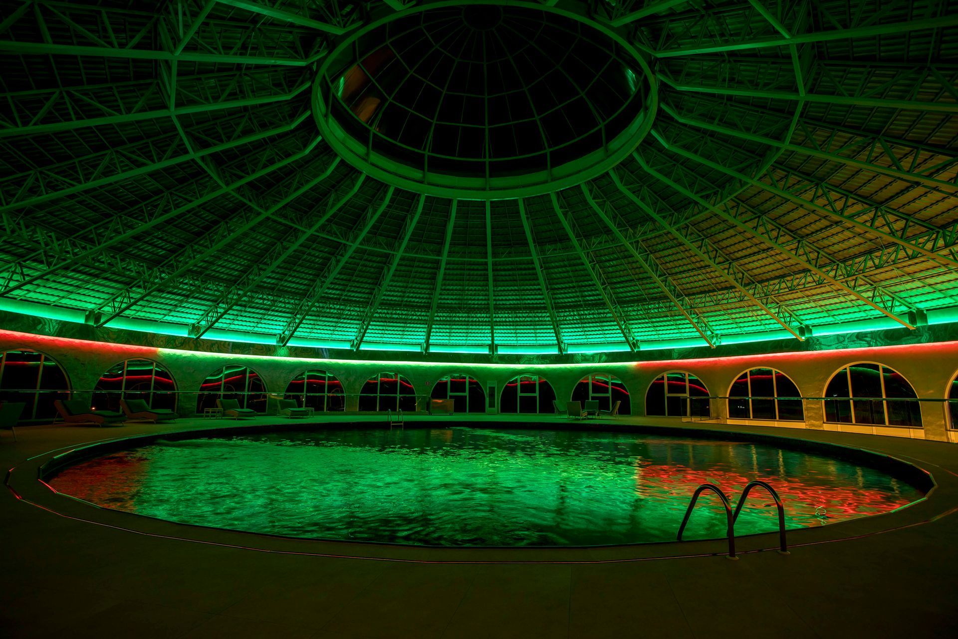 Piscina redonda sob um teto abobadado, iluminada com luzes verdes e vermelhas.