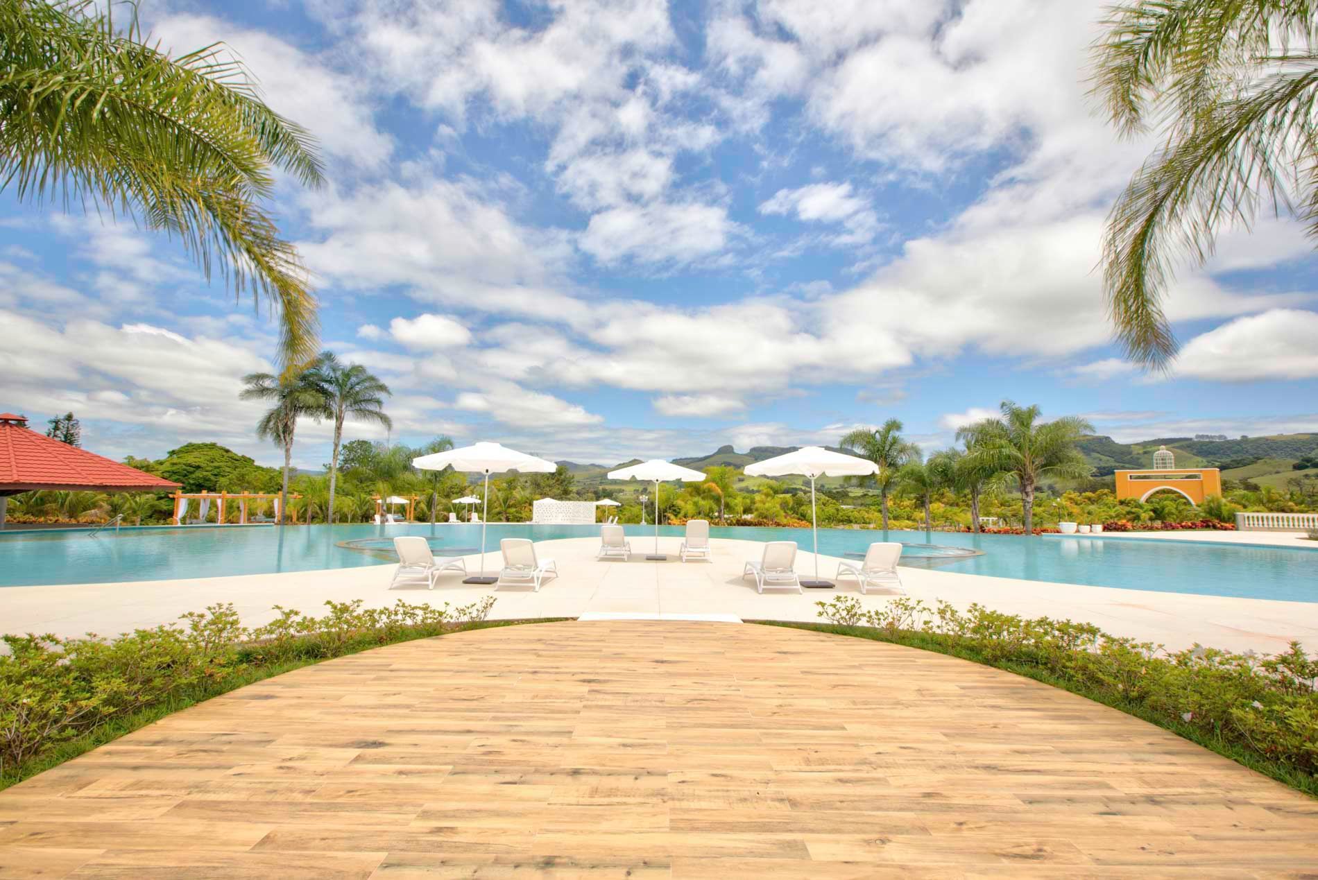 Espreguiçadeiras e guarda-sóis à beira da piscina sob um céu azul brilhante com palmeiras.