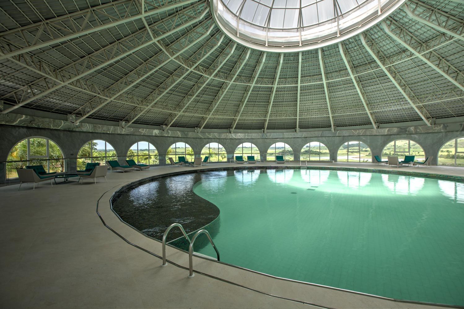 Piscina coberta sob um teto abobadado com janelas em arco e espreguiçadeiras.