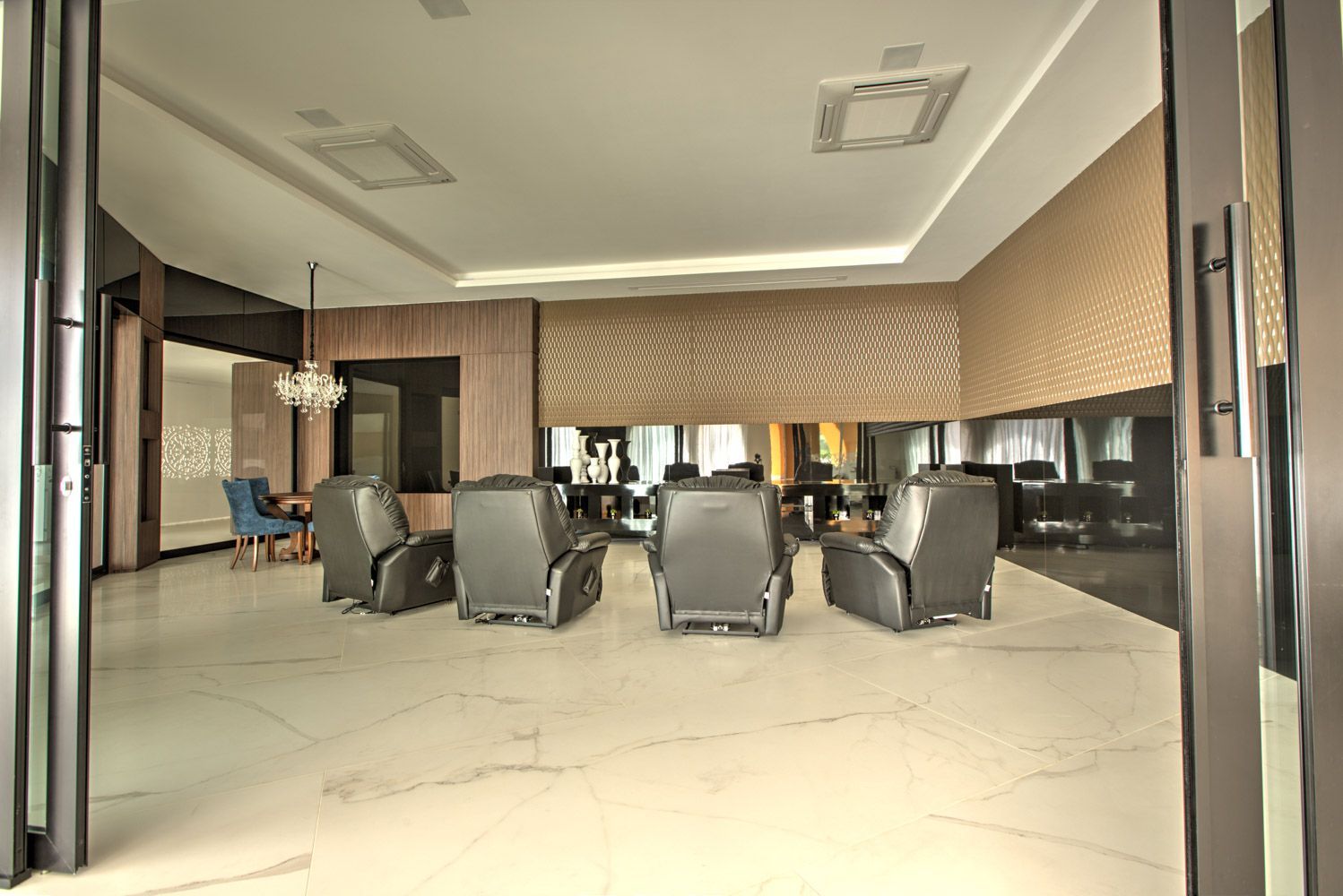 Sala de estar com poltronas reclináveis ​​cinza, piso de cerâmica branca, parede espelhada e portas abertas.