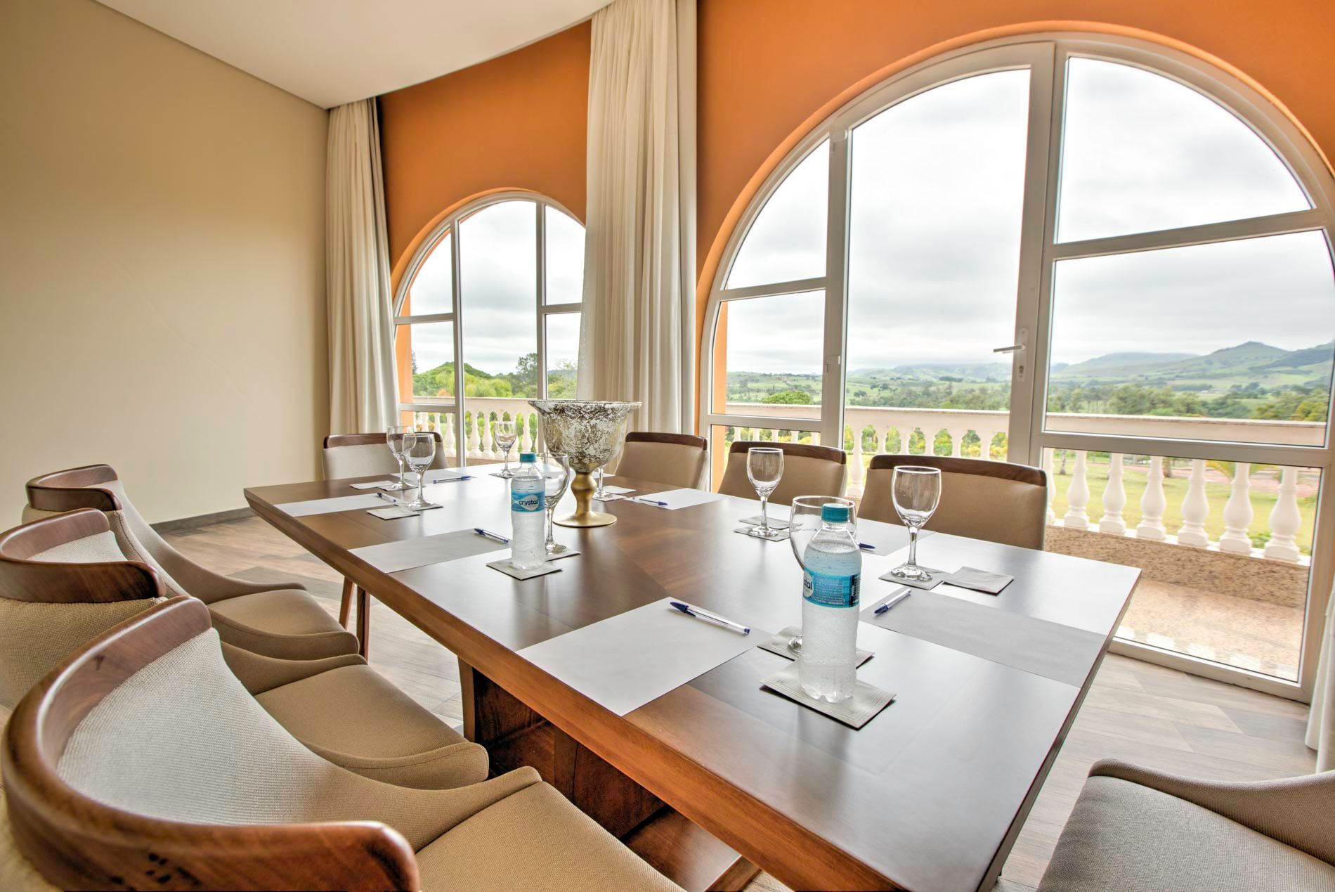 Sala de reuniões com grandes janelas em arco com vista para uma paisagem cênica, mesa posta para uma reunião.