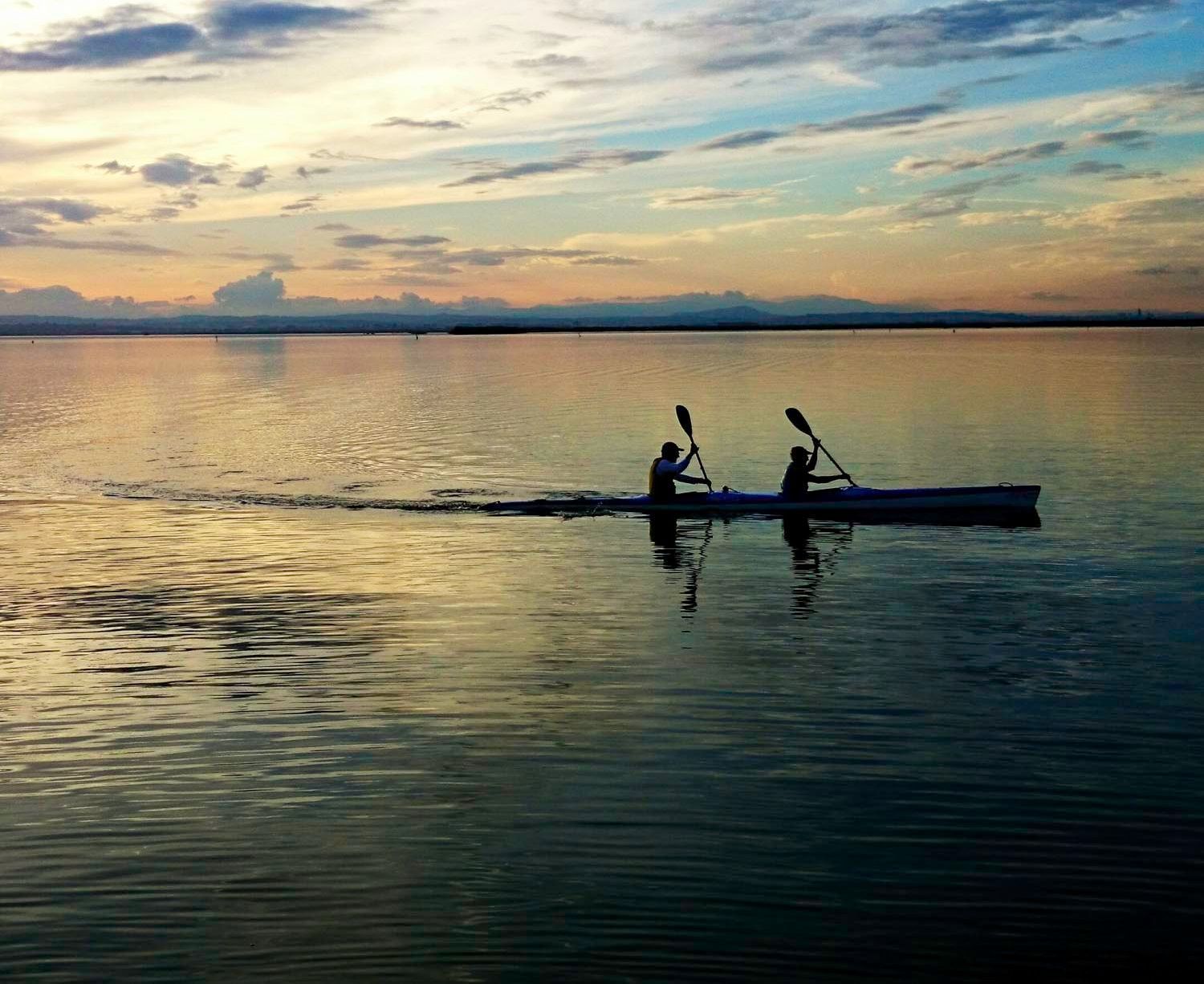 Duas pessoas andando de caiaque em águas calmas ao pôr do sol.
