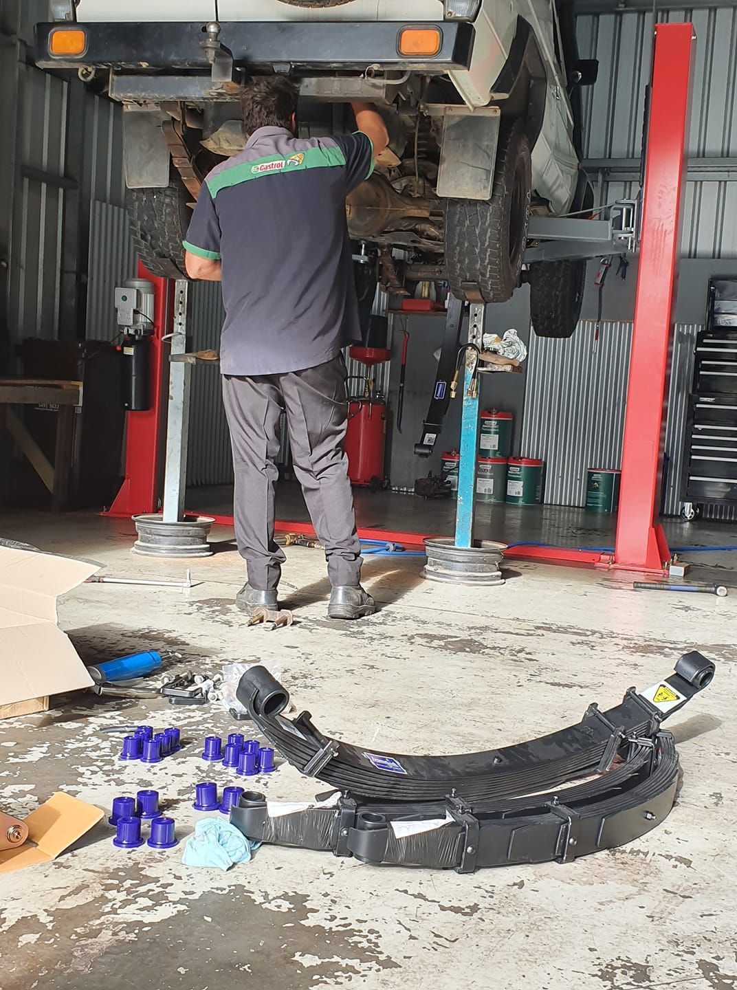 Mechanic working under a lifted vehicle in a garage, with new suspension parts on the floor. — Adam's Automotive Centre in Nambour, QLD
