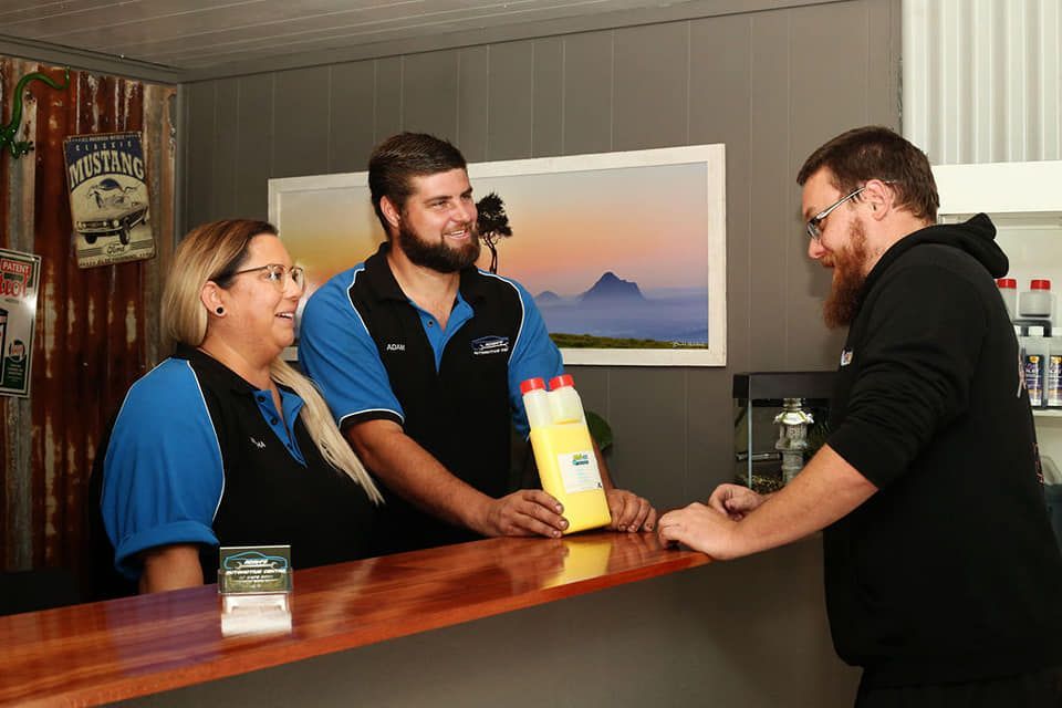 Two people behind a counter with a customer, holding a box in a shop. — Adam's Automotive Centre in Nambour, QLD