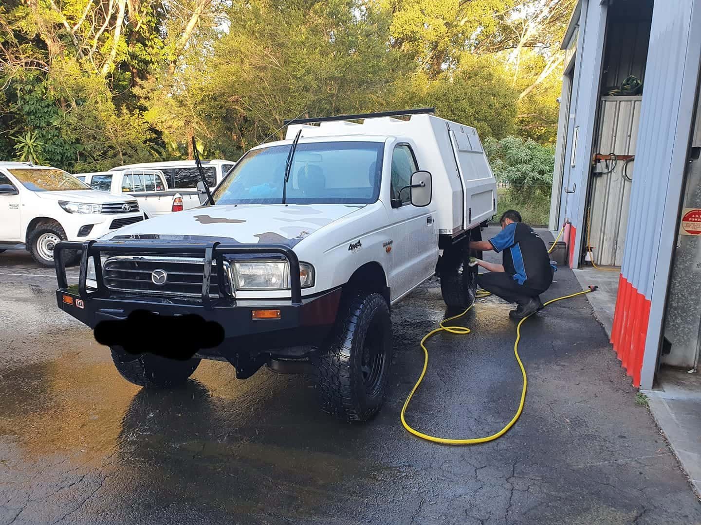 White pickup truck with canopy parked at a car wash, being cleaned by a person. — Adam's Automotive Centre in Nambour, QLD