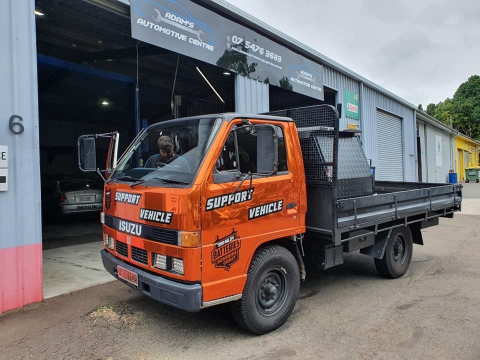 Orange Isuzu Support Vehicle parked outside a garage, with a driver visible. — Adam's Automotive Centre in Nambour, QLD