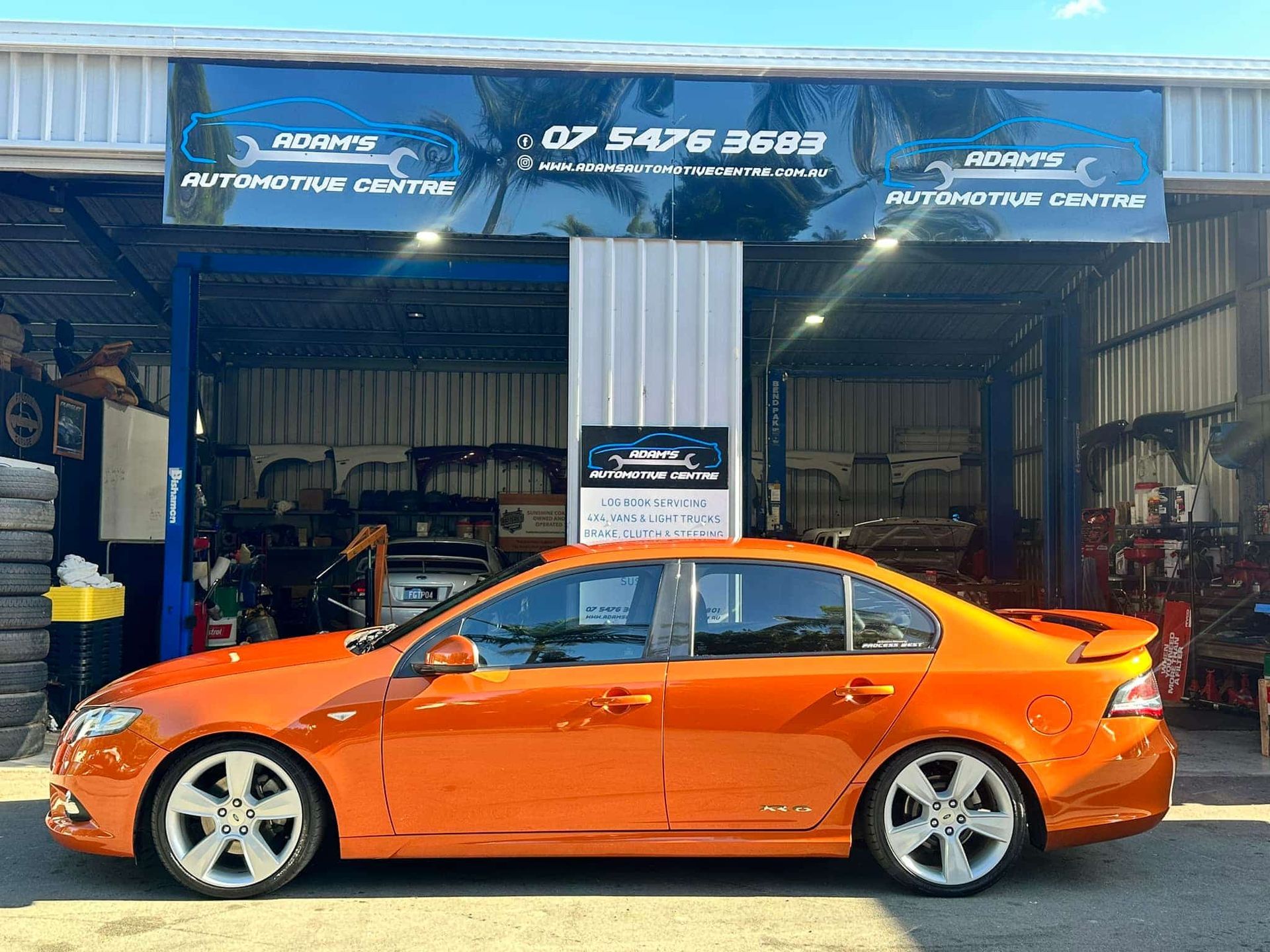 Orange car in front of an auto shop. Shop sign reads 