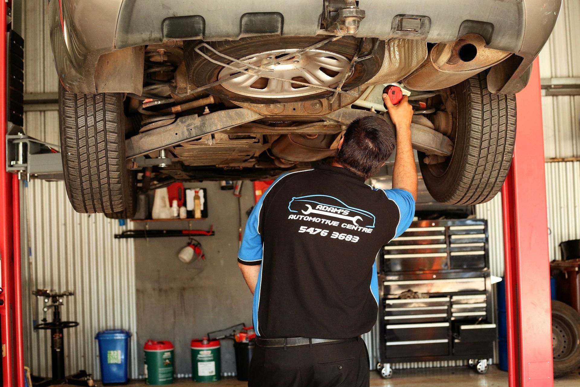 Mechanic Under a Car on a Lift Using a Flashlight — Adam's Automotive Centre in Nambour, QLD