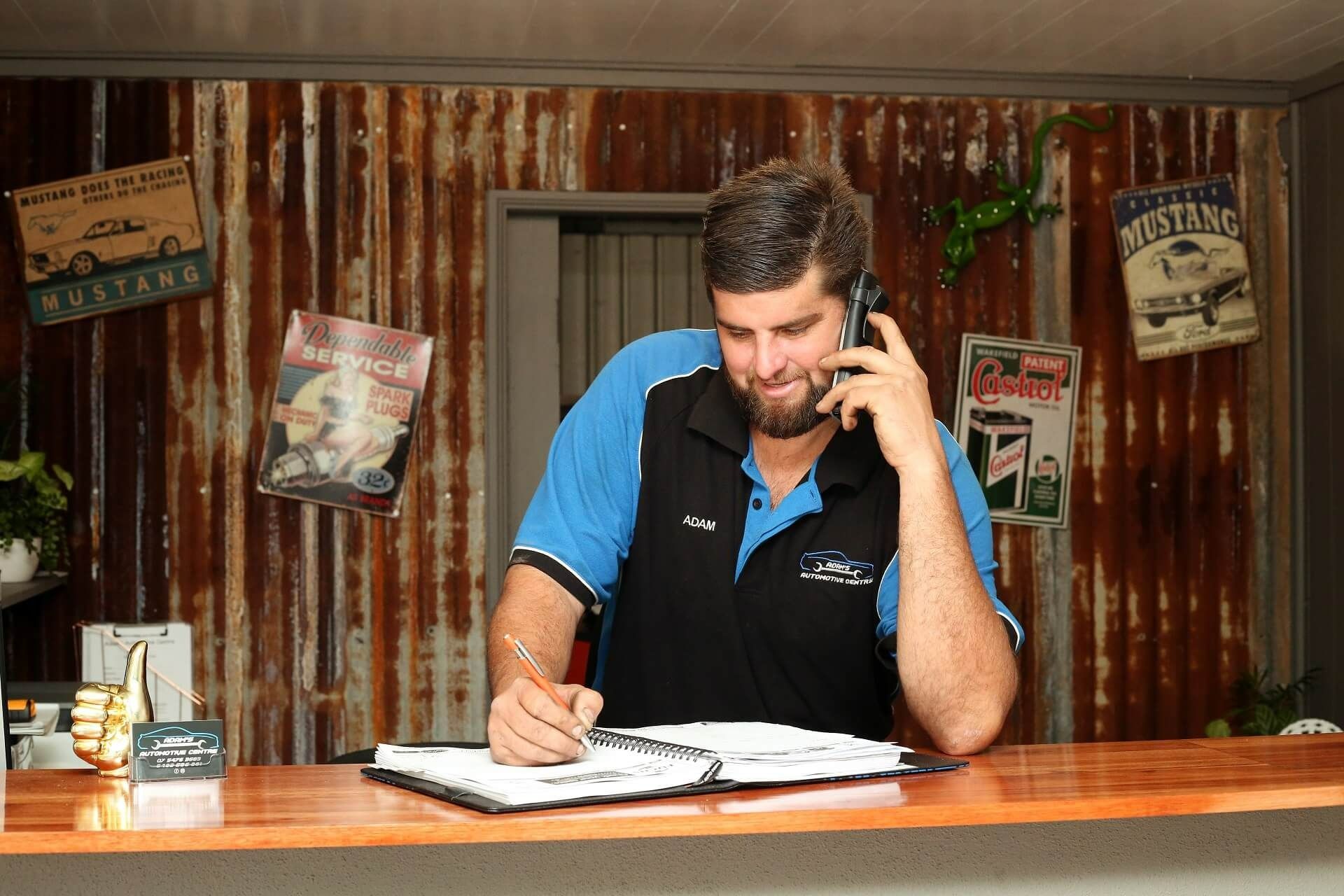 Man Talking on Phone Writing at a Counter With Rusty Metal Wall — Adam's Automotive Centre in Nambour, QLD