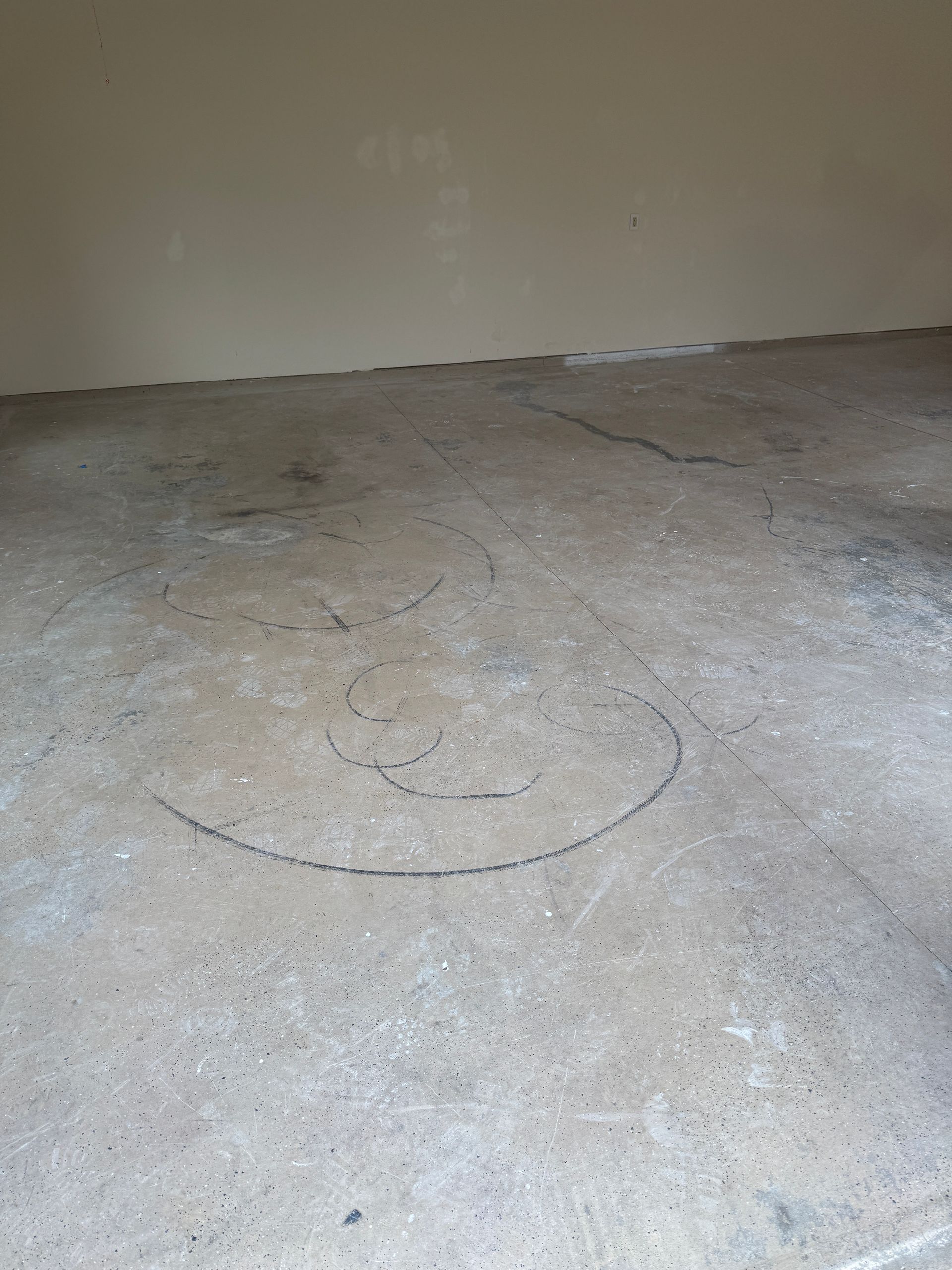 Concrete floor with black lines and marks, potentially from tire tracks, indoors.