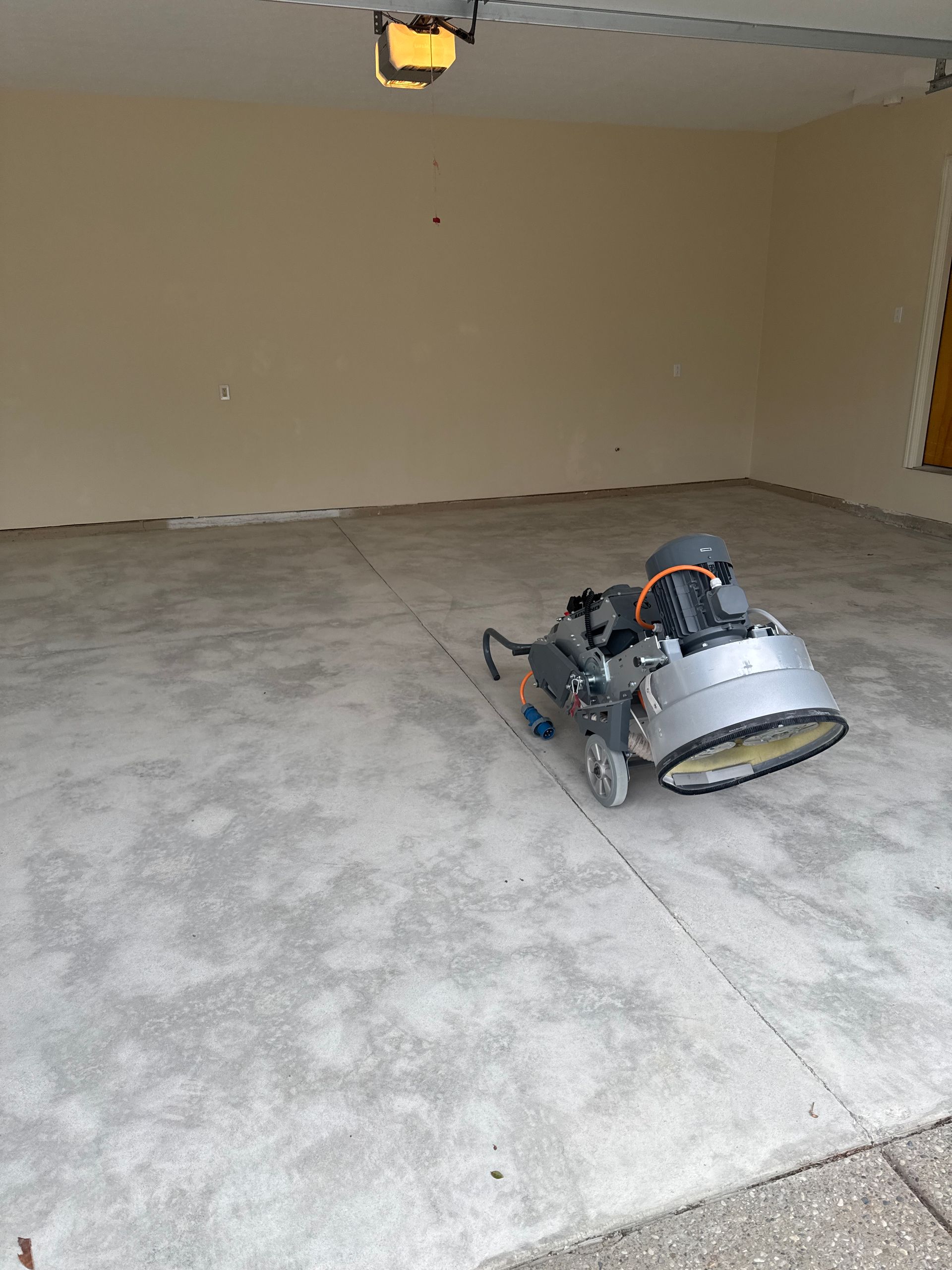 Garage floor being ground with a concrete grinder; beige walls, gray floor.