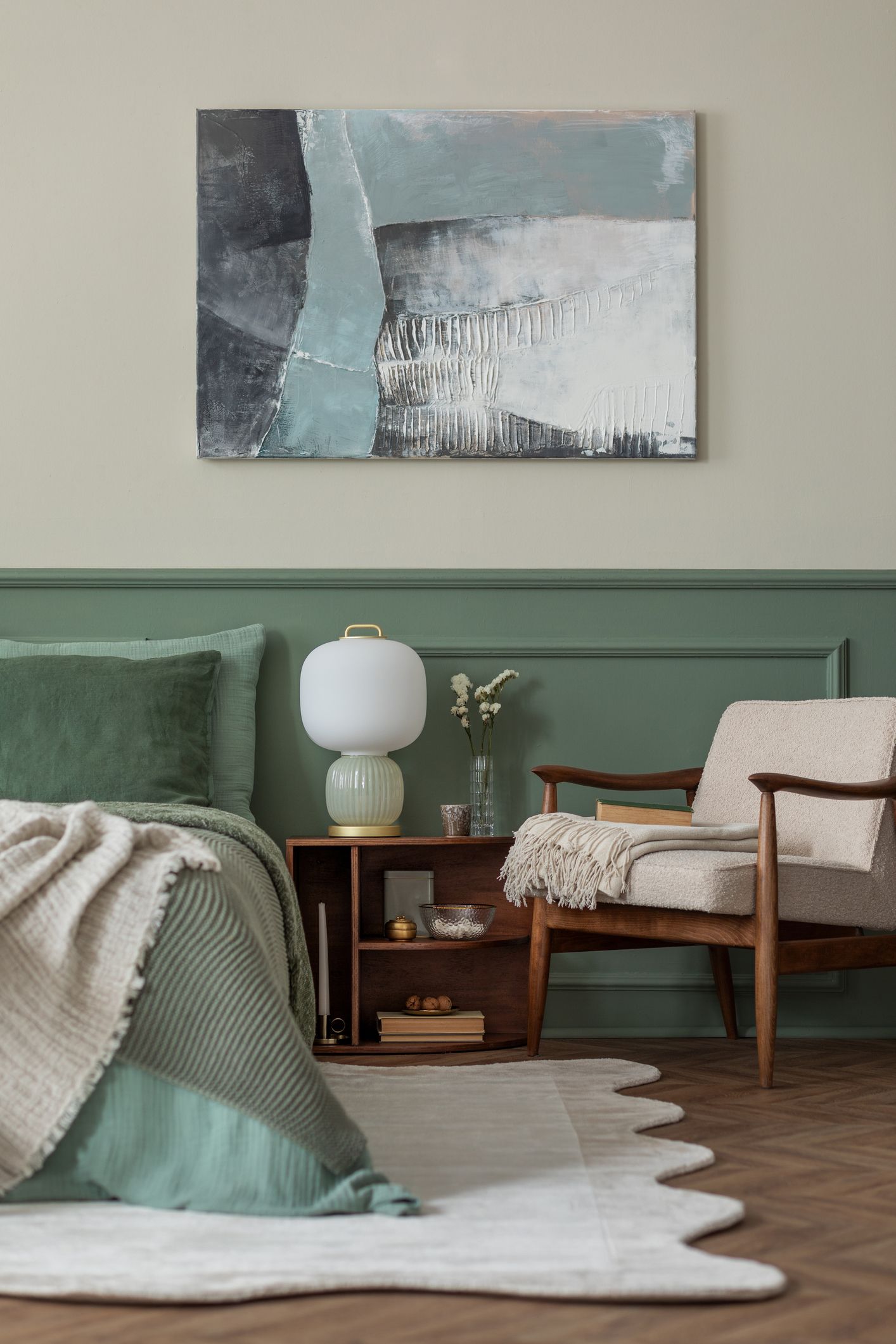 Bedroom with green walls, a bed with cream-colored throw, and a wooden chair. Abstract art above the nightstand.
