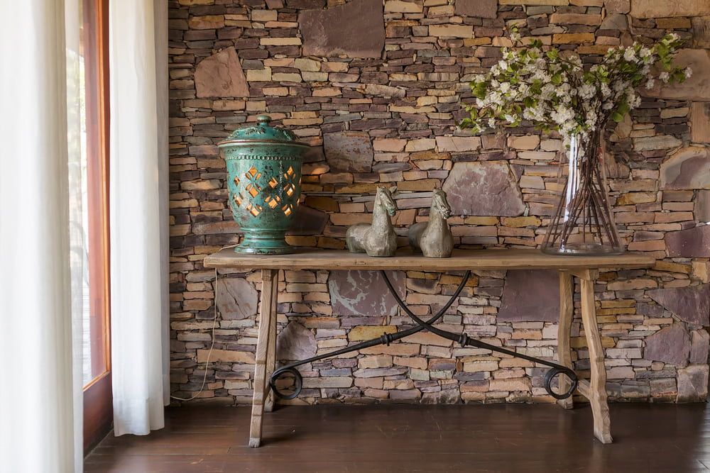 A Wooden Table With a Vase of Flowers on It in Front of a Stone Wall — Tileflair in Mitchell, ACT