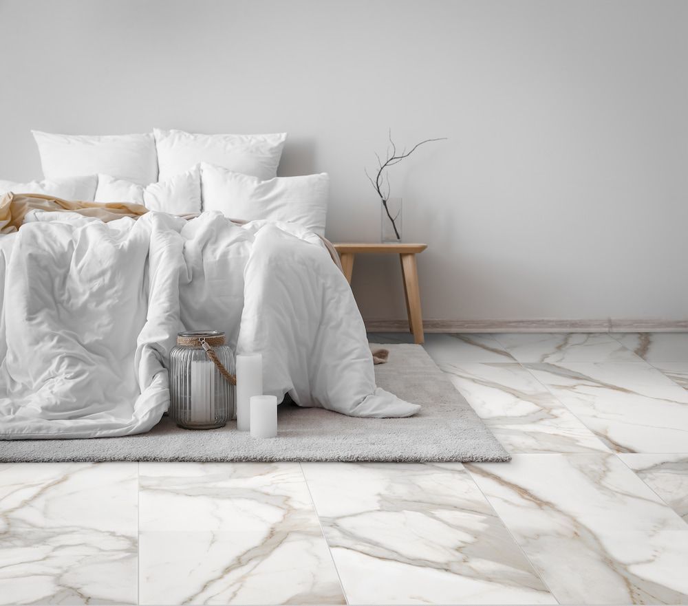 A Bed With White Sheets and Pillows is Sitting on a Marble Floor in a Bedroom — Tileflair in Mitchell, ACT