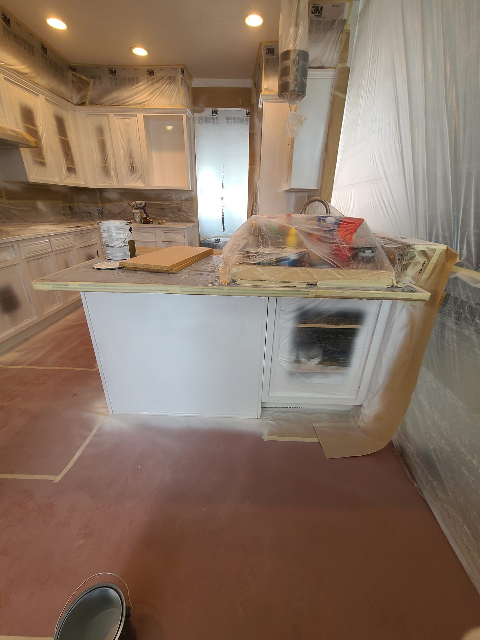 A kitchen with white cabinets and a red floor is being painted.