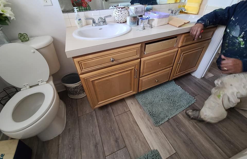 A man is kneeling in a bathroom next to a toilet and sink.