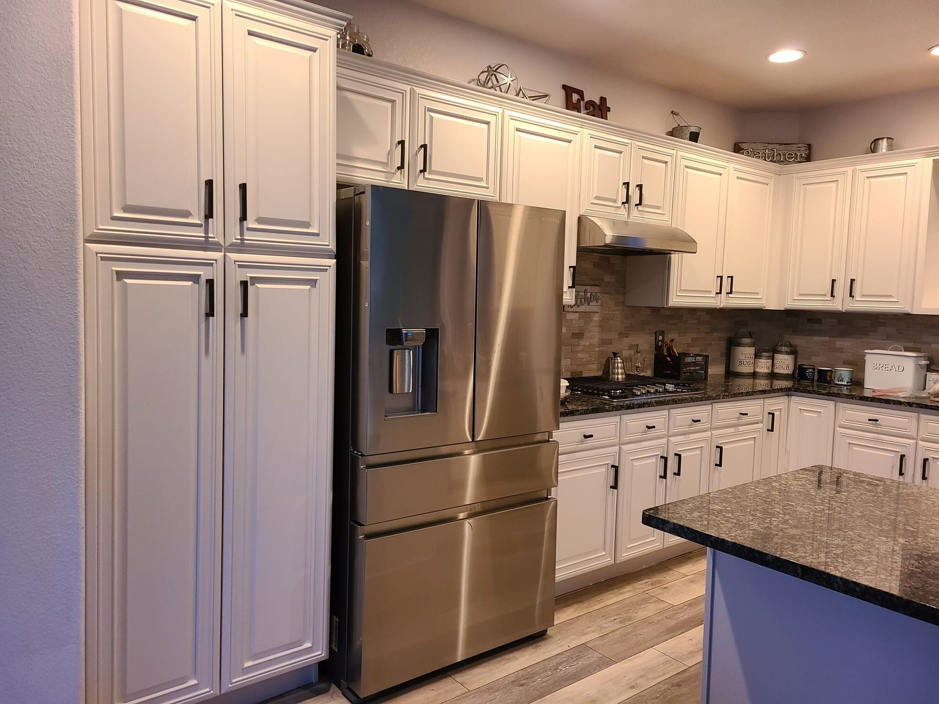 A kitchen with white cabinets and a stainless steel refrigerator.