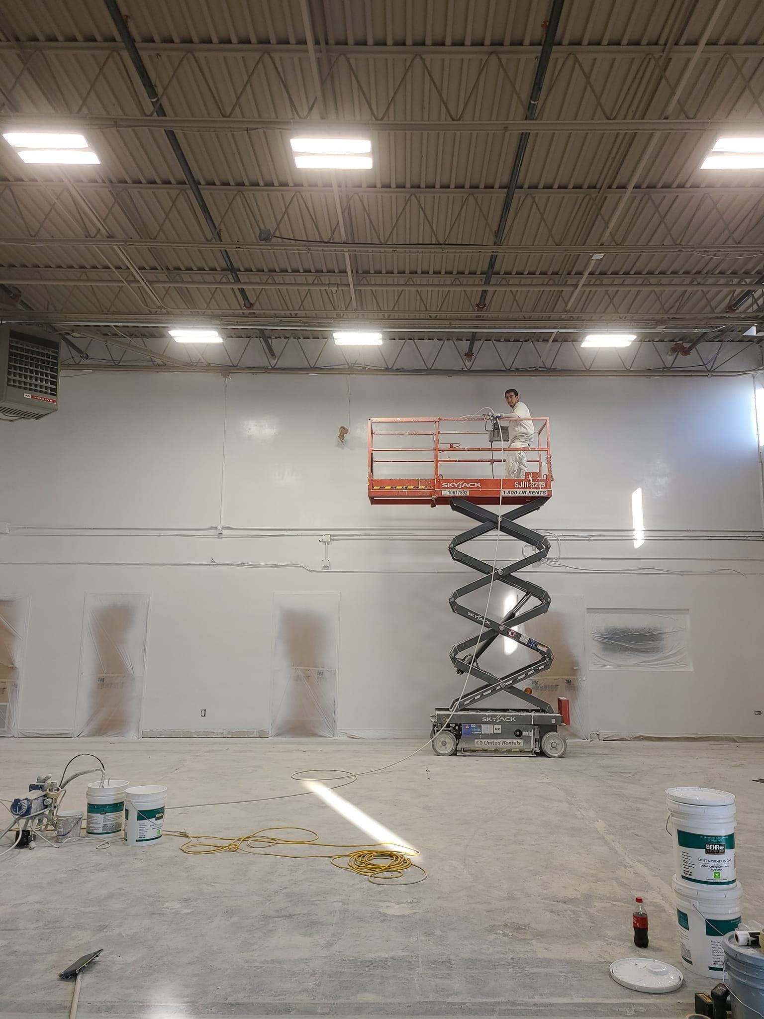 A man is standing on a scissor lift in a large room.