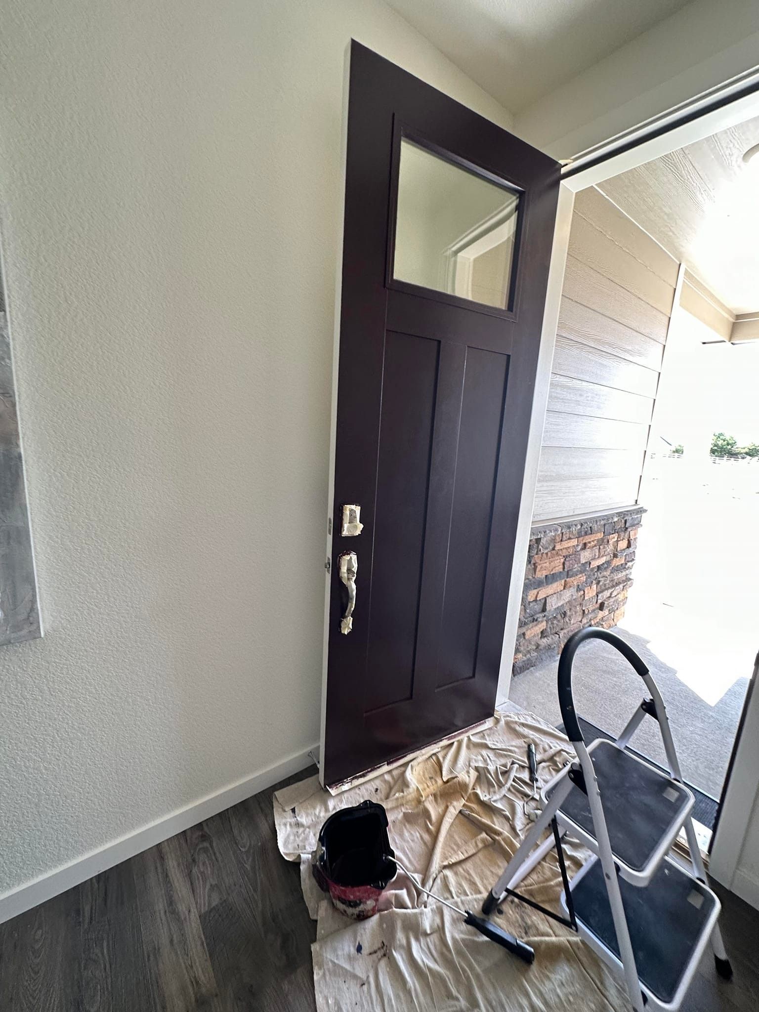 A door is being painted in a room with a ladder.