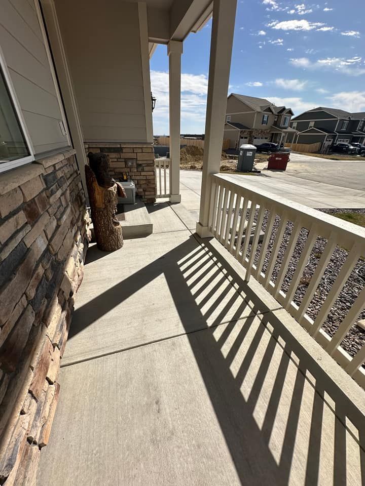 A porch with a white railing and shadows on the concrete.